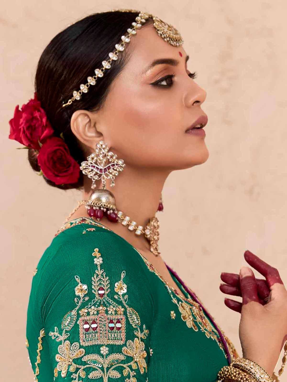 Woman in green embroidered ethnic wear with gold jewelry and red rose hair accessory