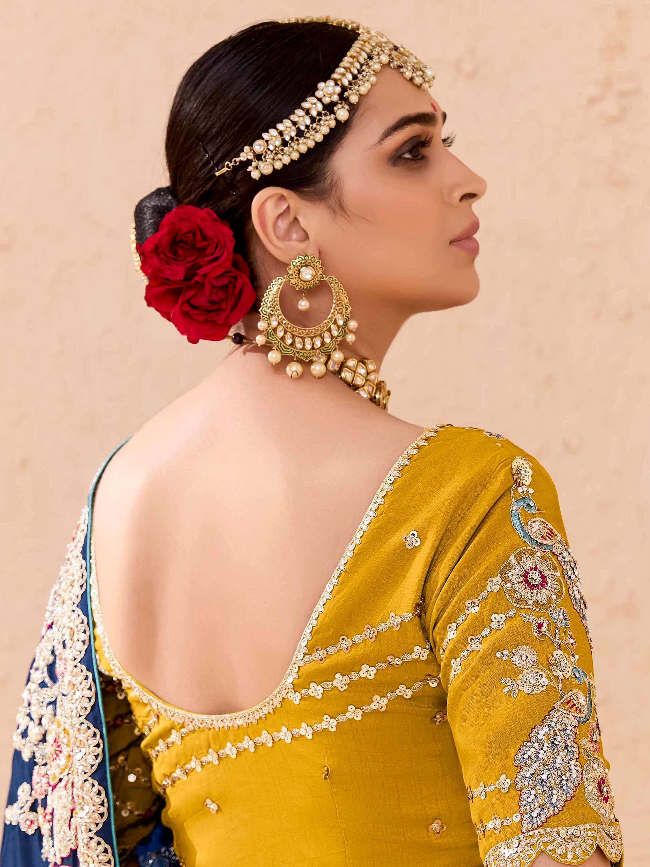 Woman in mustard yellow embroidered lehenga choli with pearl jewelry and red rose hair accessory