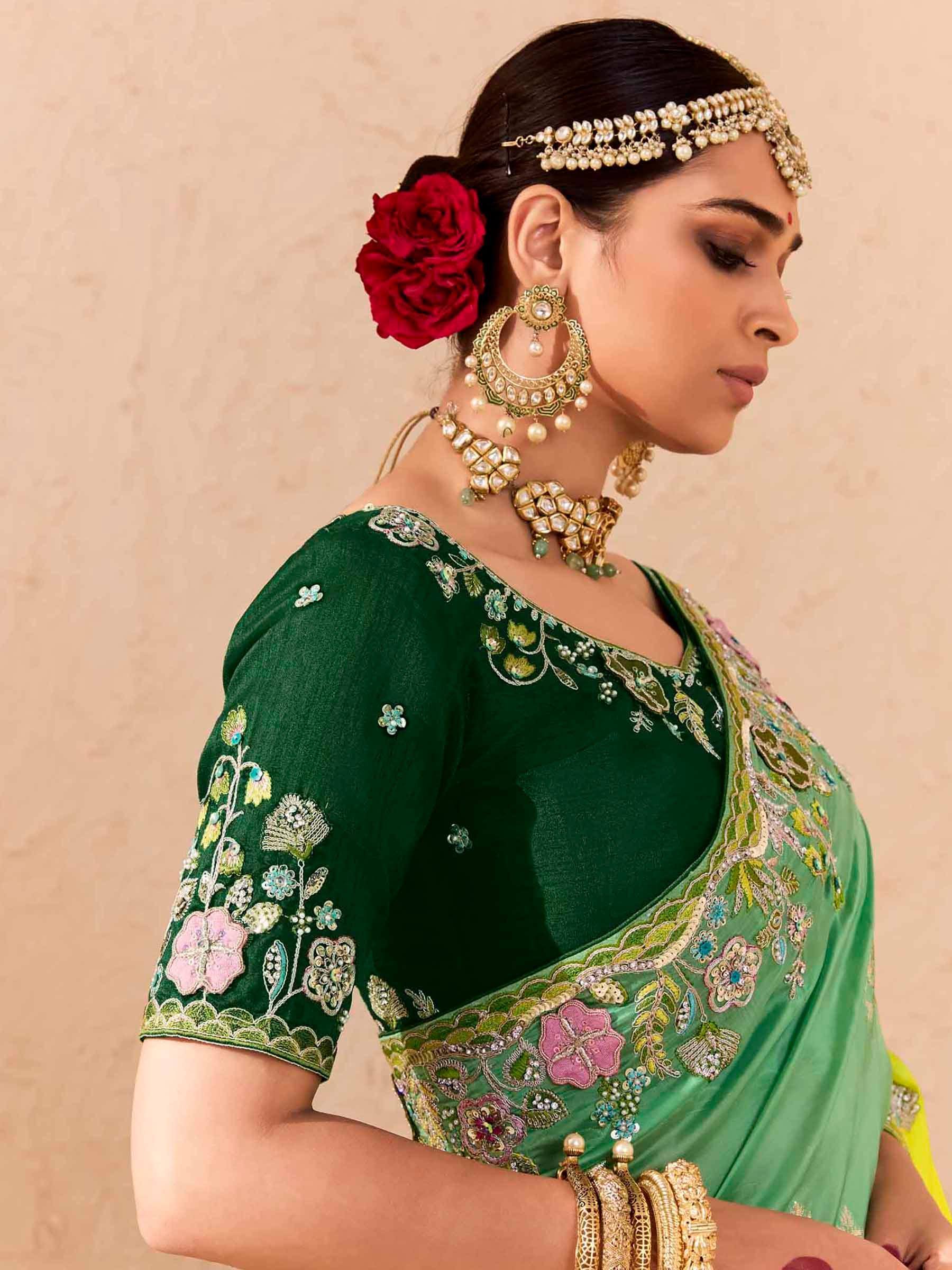 Emerald green embroidered saree with floral motifs, traditional jewelry, and red rose hair accessory