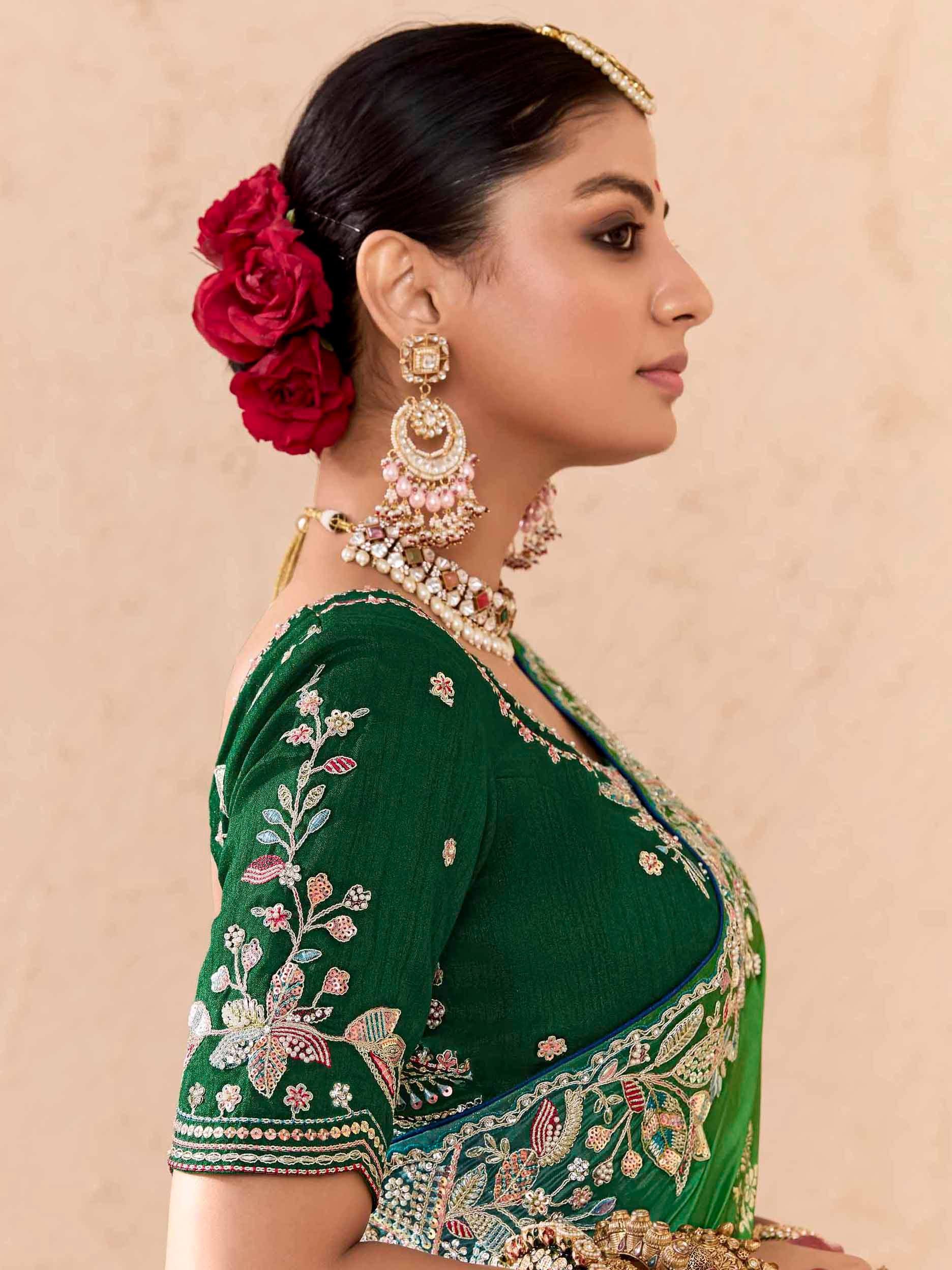 Woman in green embroidered saree with floral design, red roses in hair, and traditional Indian jewelry
