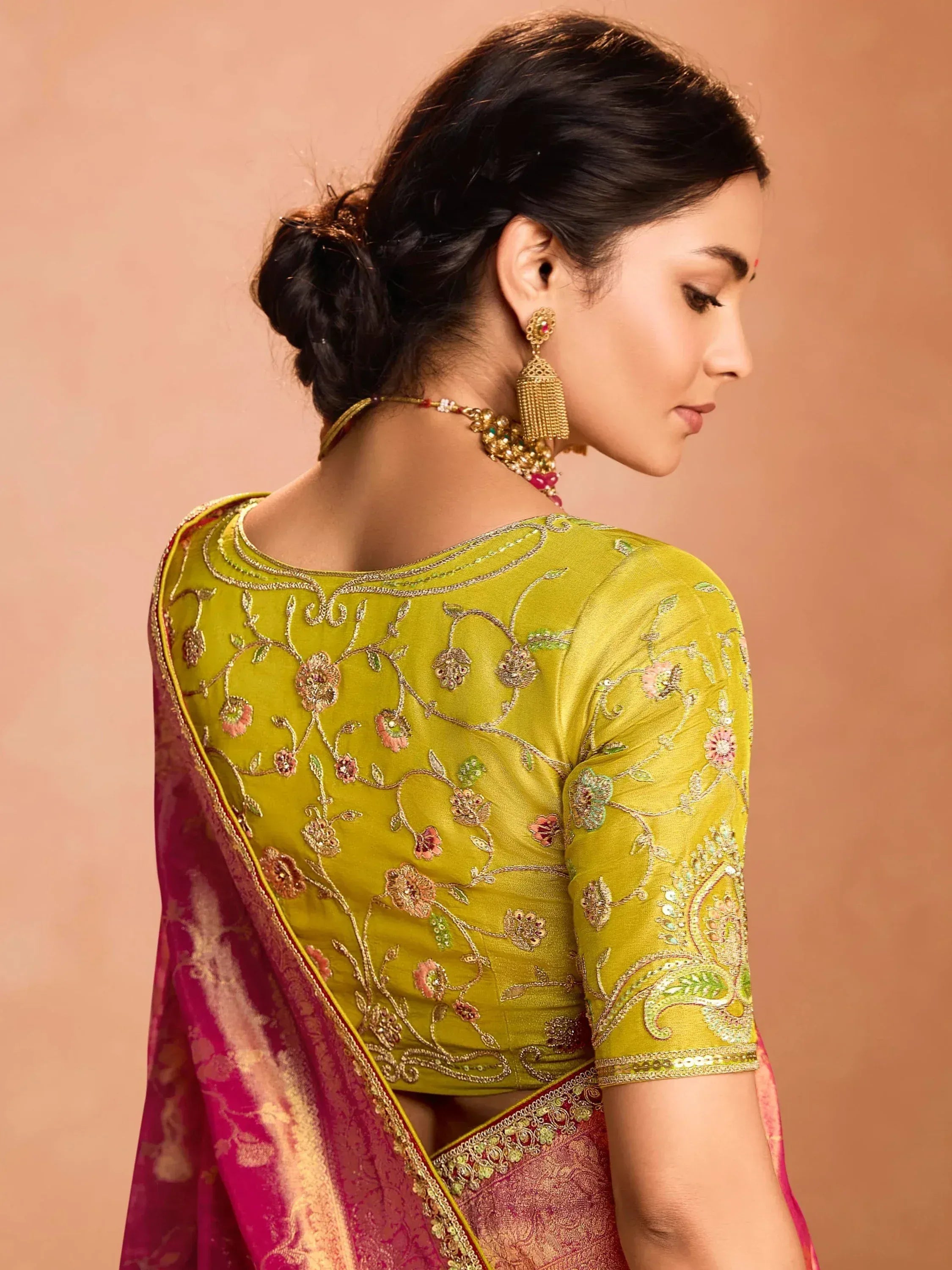 Woman in yellow embroidered saree blouse with floral design, paired with pink saree, traditional Indian ethnic wear