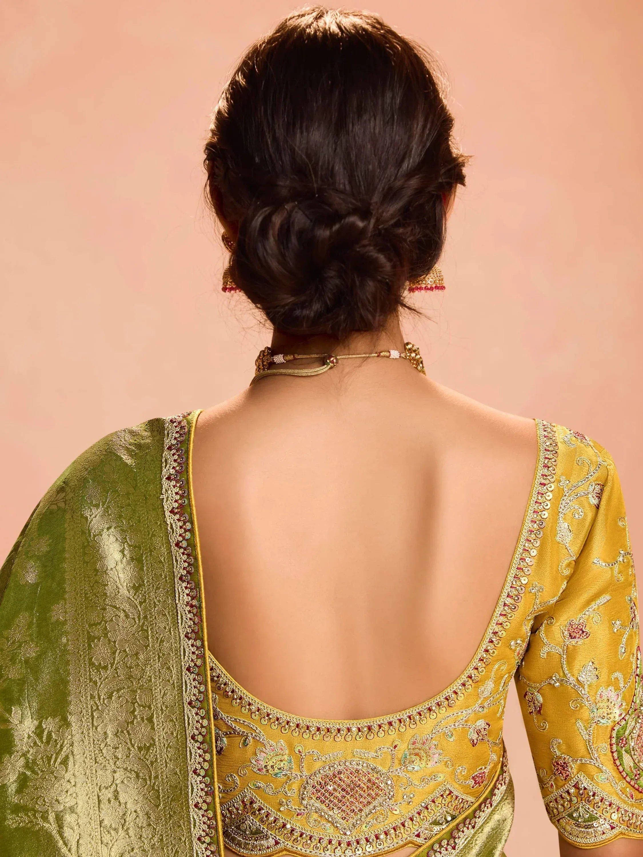 Back view of woman in yellow embroidered designer lehenga choli with green dupatta, showcasing intricate back detailing.