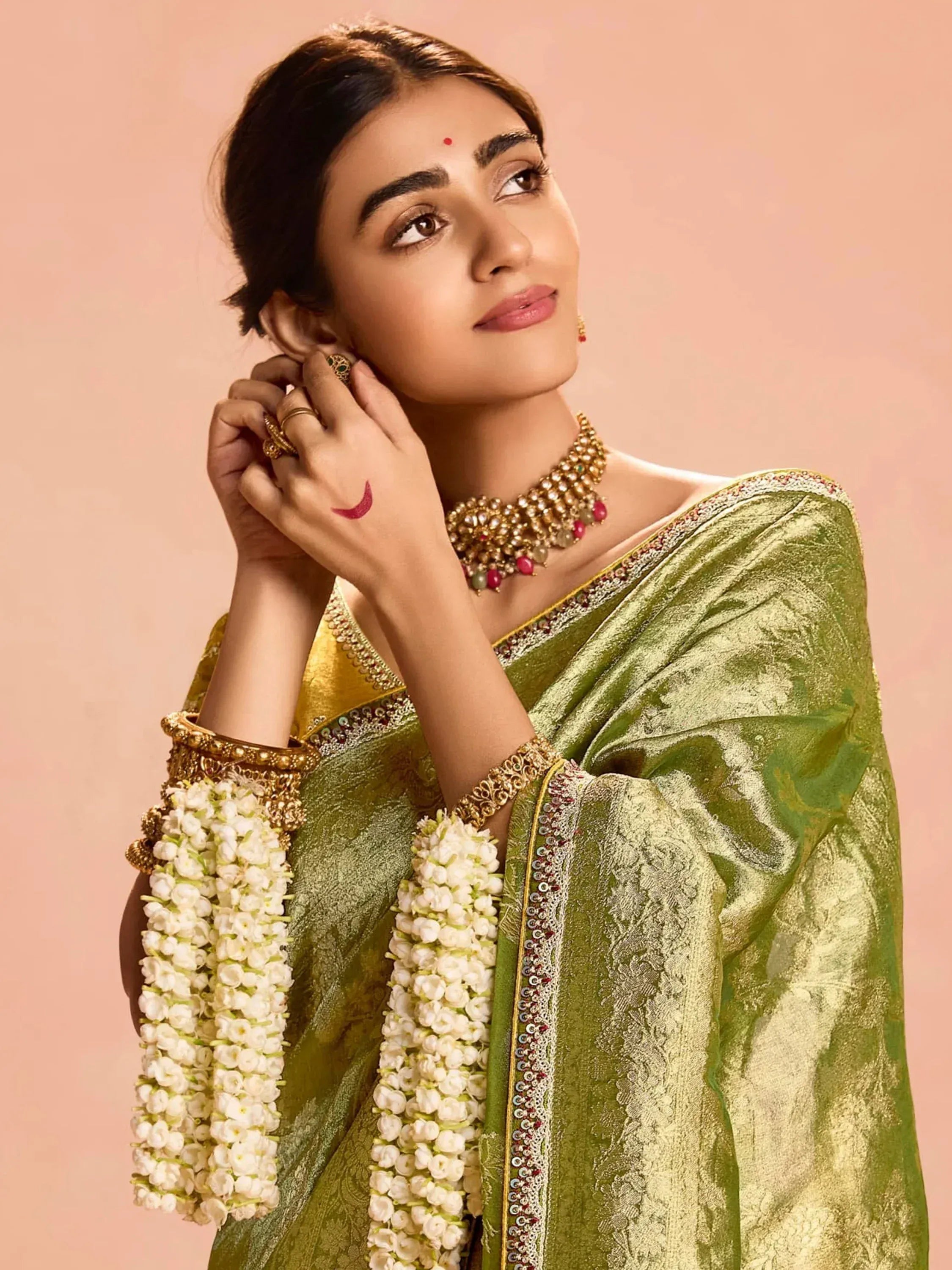Elegant woman in green designer saree with gold jewelry and floral garlands, showcasing Indian ethnic wear.