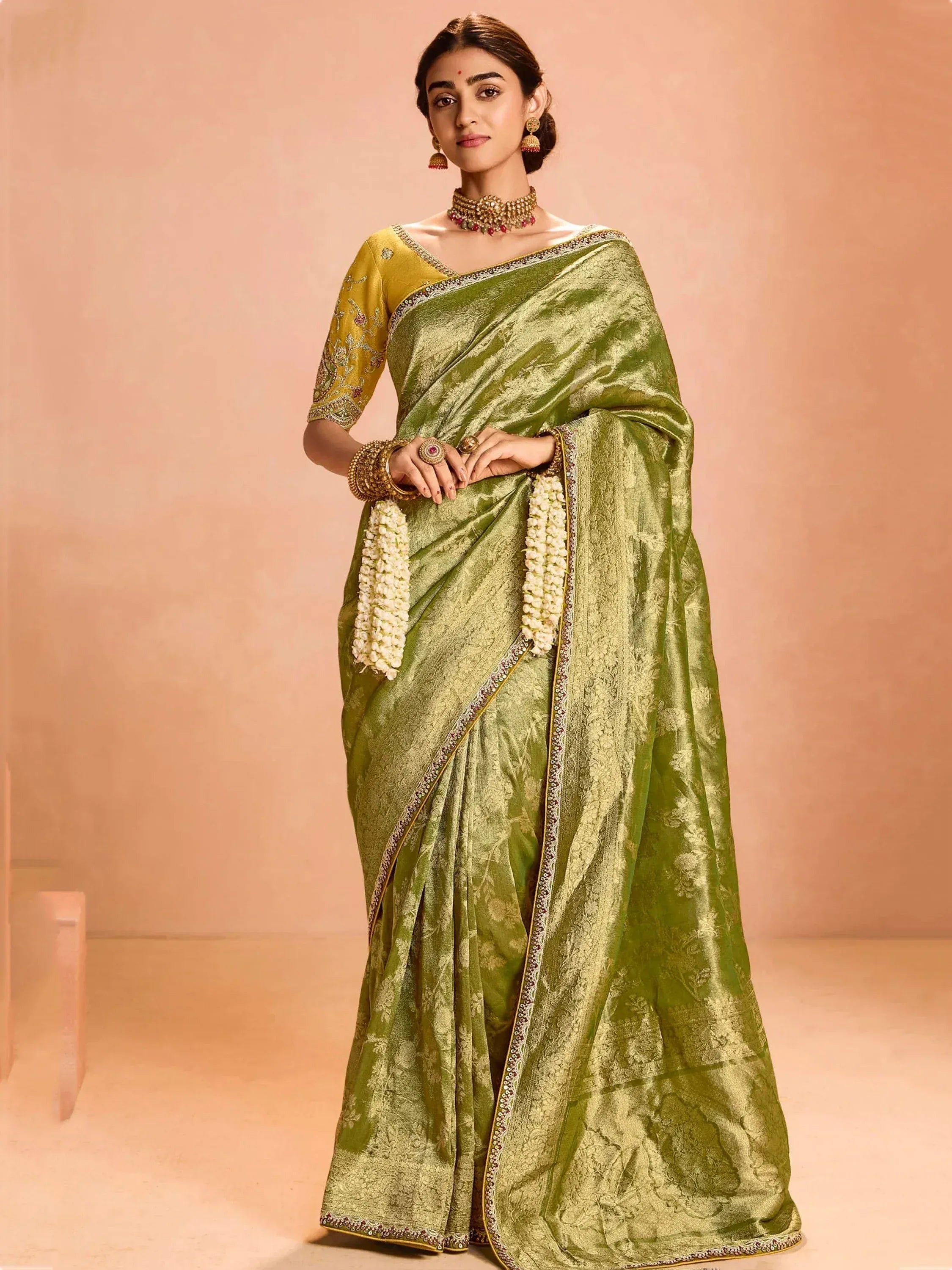 Elegant green designer saree with golden embroidery and floral border, paired with traditional jewelry.