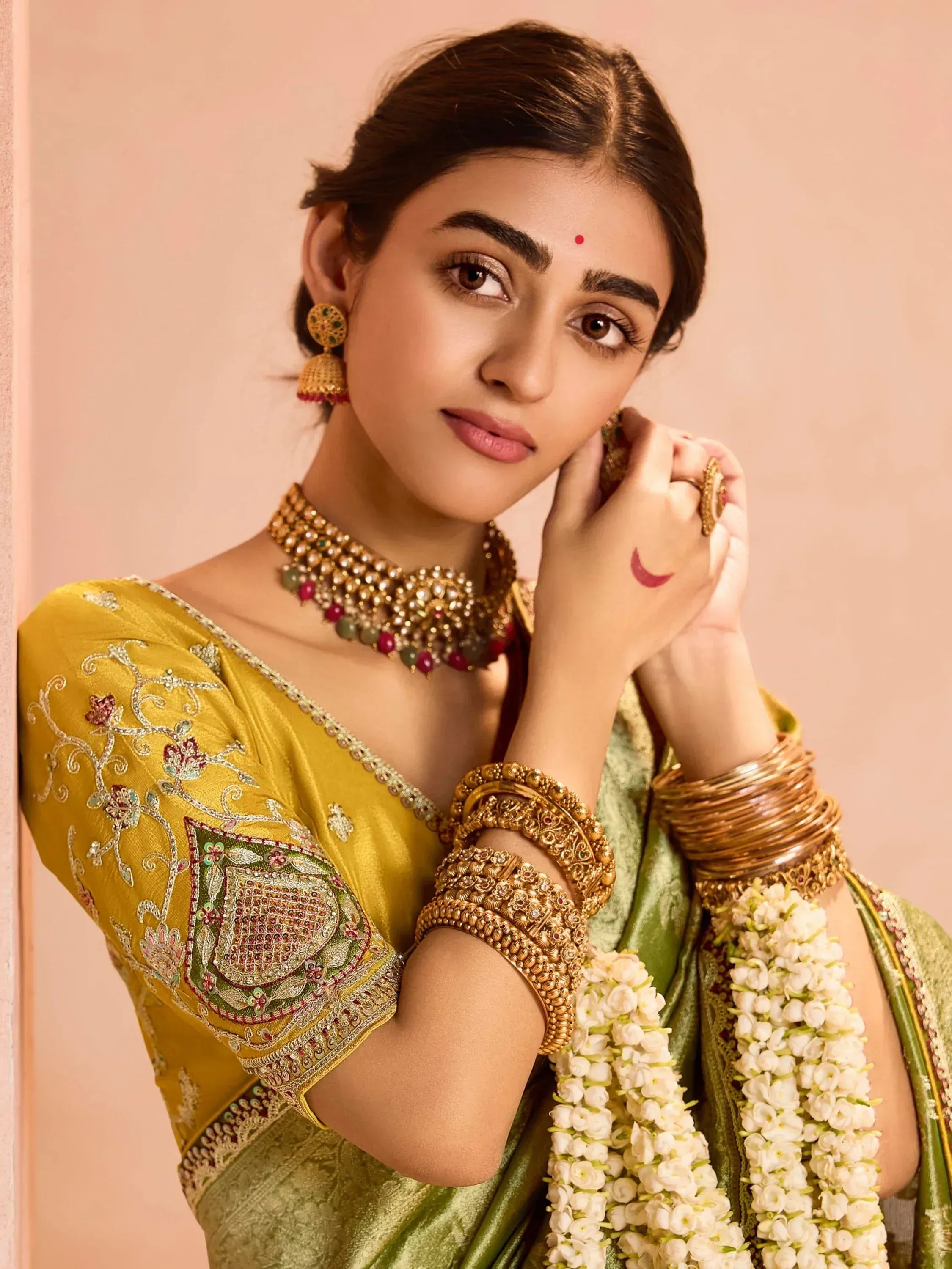Elegant woman in yellow and green embroidered saree with gold jewelry and floral garlands