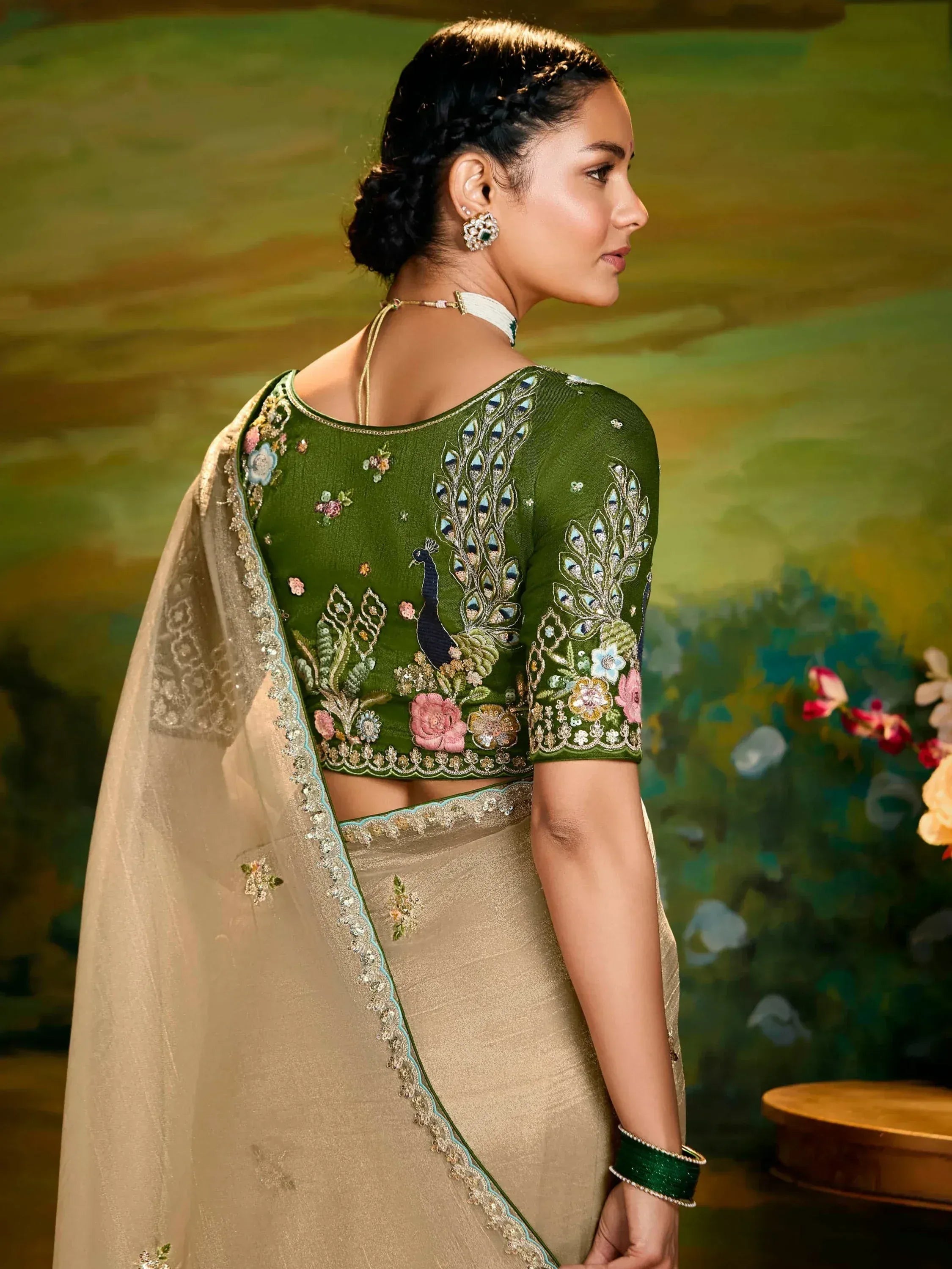 Green peacock-embroidered saree blouse with floral details, paired with beige saree, perfect for ethnic occasions.