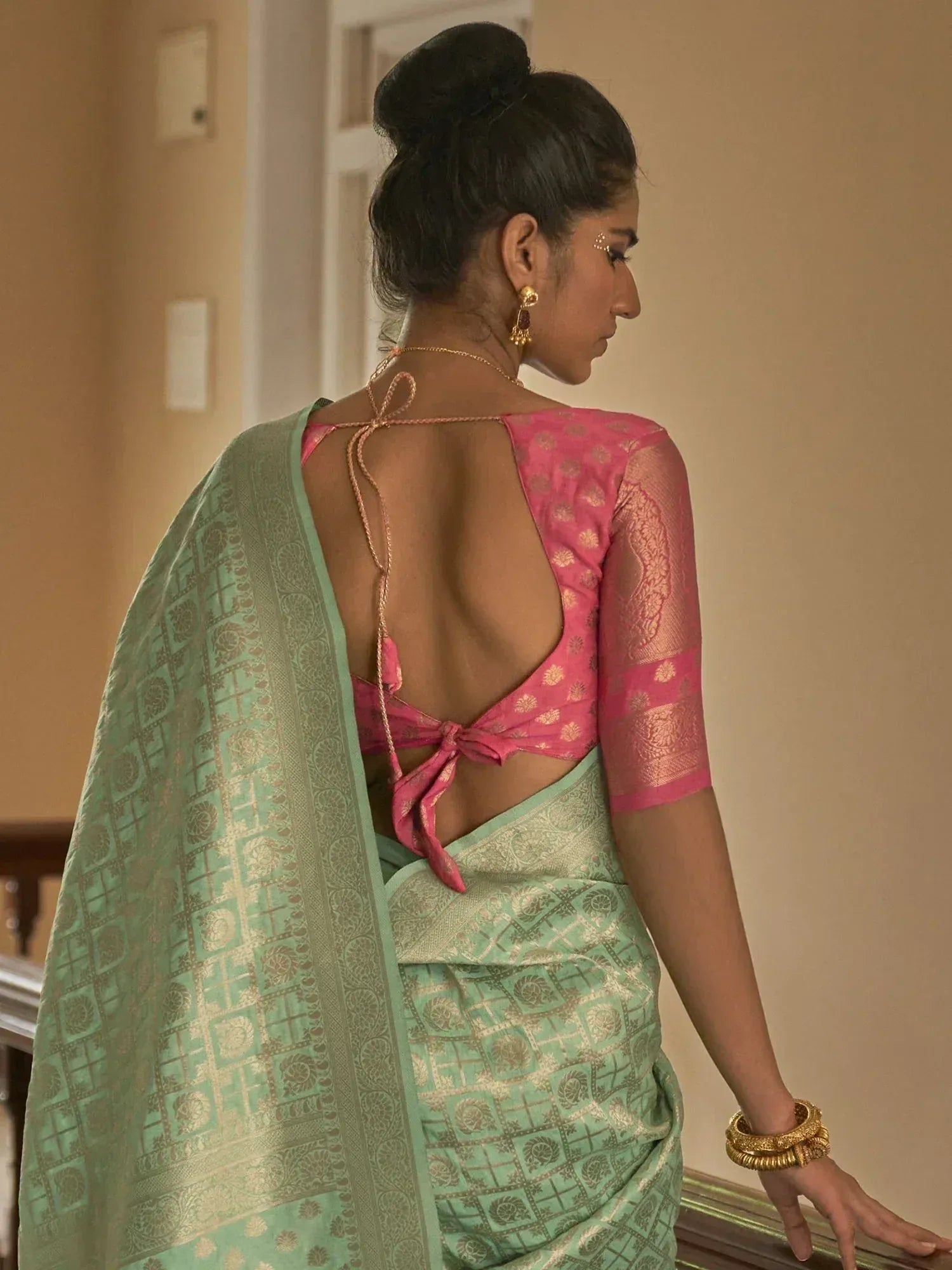 Woman in mint green saree with gold motifs and pink backless blouse, showcasing ethnic Indian wear
