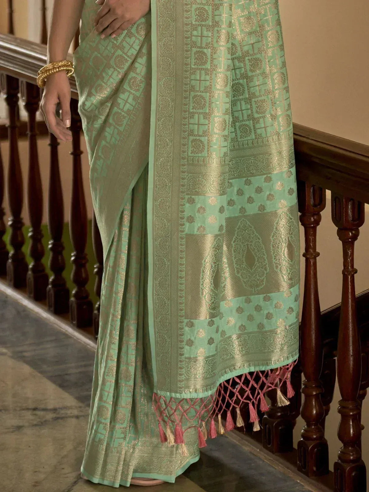 Mint green designer saree with gold zari work and pink tassels, perfect for ethnic occasions