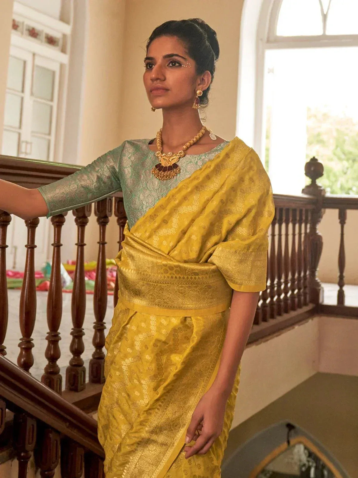 Yellow silk saree with gold embroidery, paired with green blouse and traditional jewelry, perfect for Indian ethnic occasions.