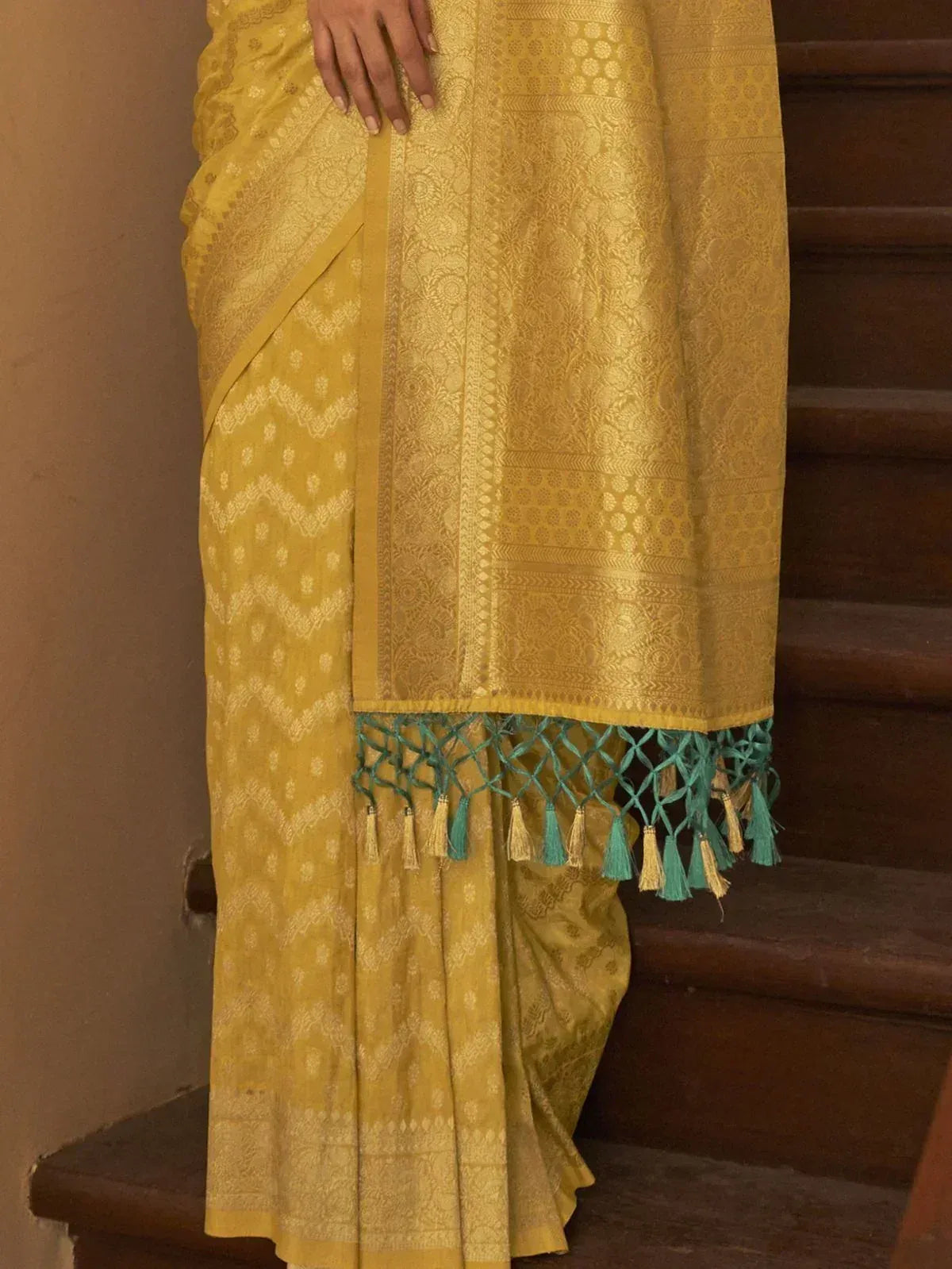 Yellow ethnic saree with gold weave and teal tassels, styled for festive occasions