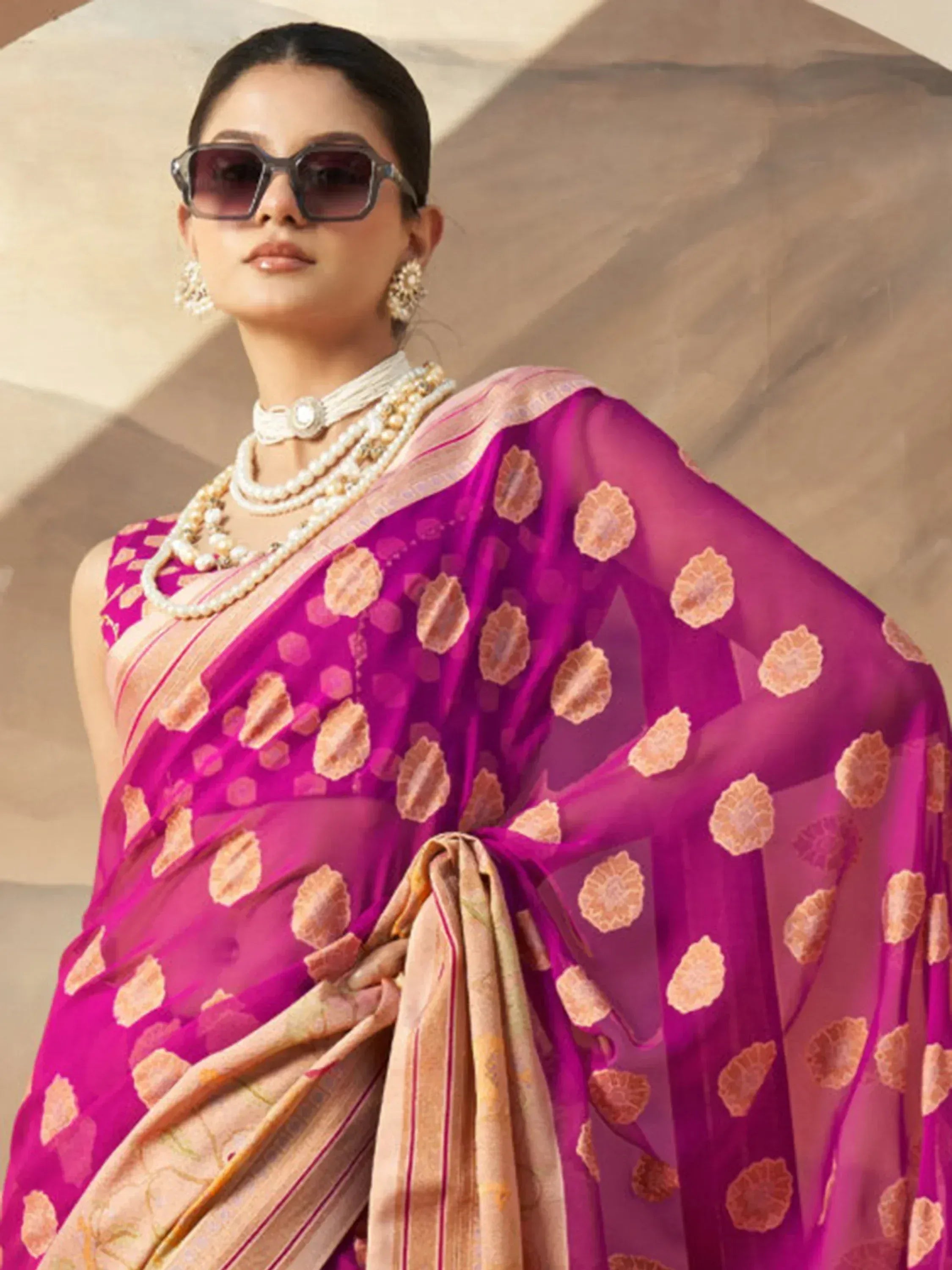 Woman in vibrant pink floral saree with pearl jewelry and sunglasses, showcasing ethnic Indian fashion.