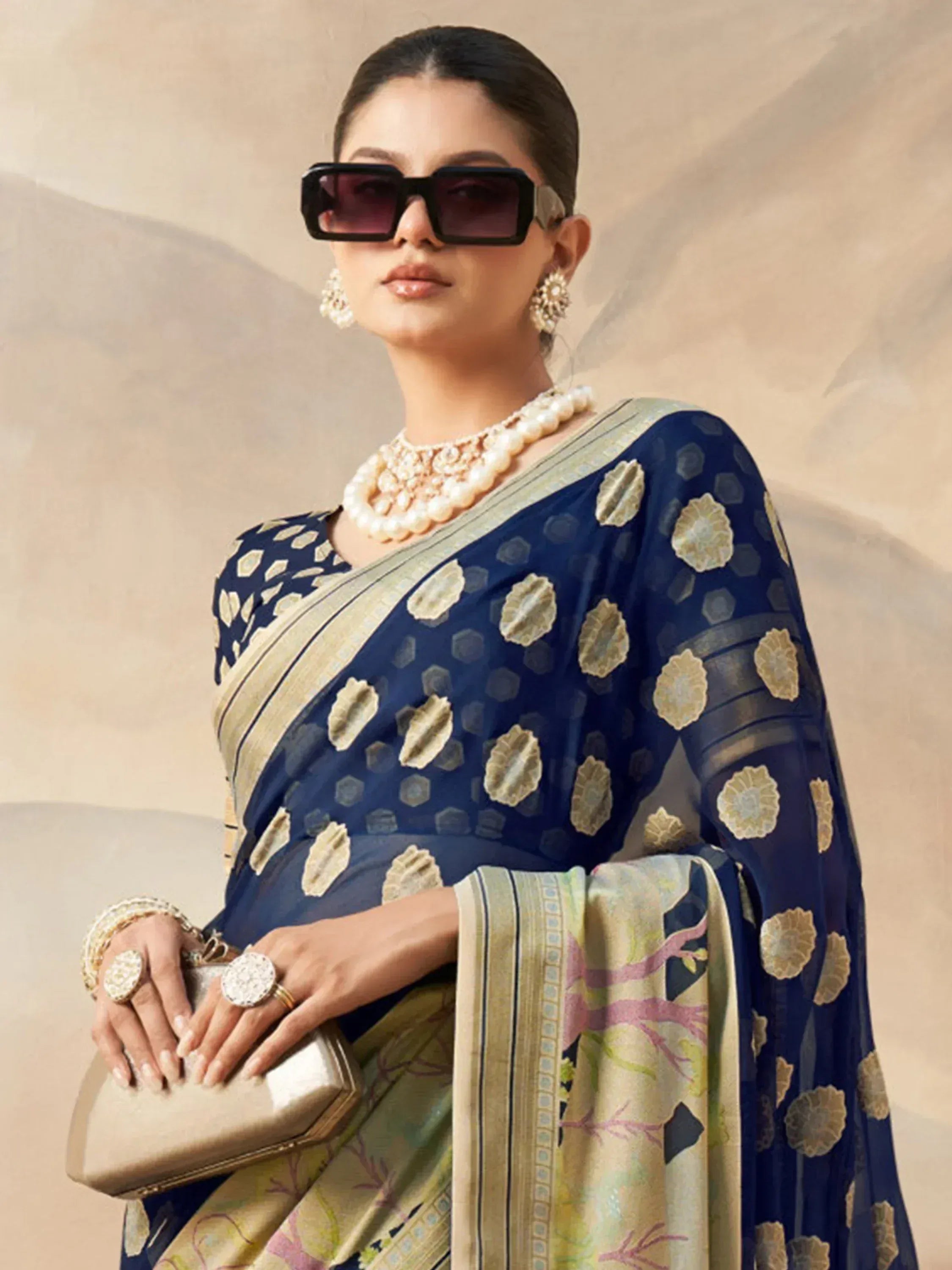 Elegant woman in navy blue floral saree with gold border, pearl jewelry, and statement sunglasses