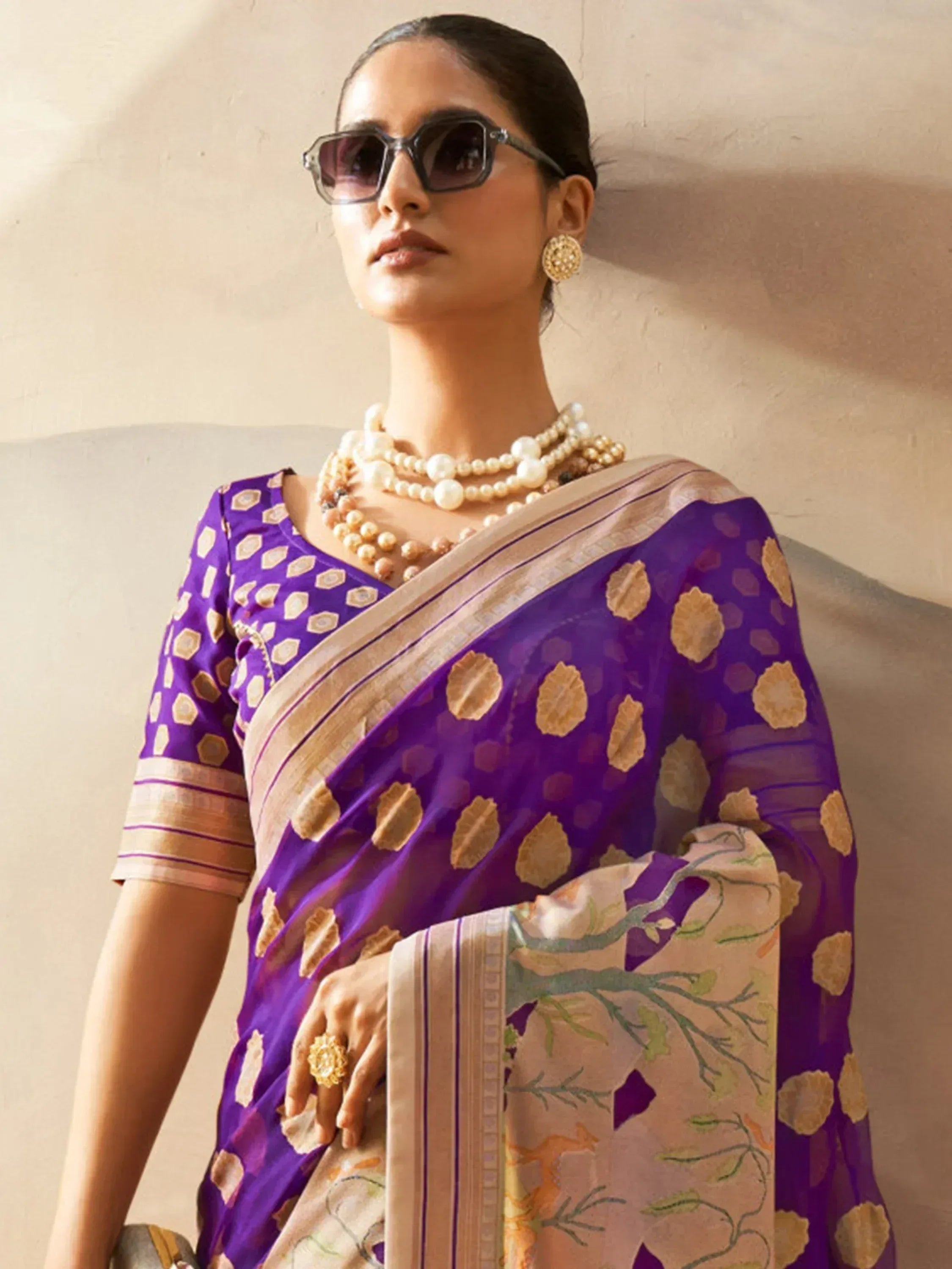 Purple printed saree with gold motifs, pearl jewelry, and sunglasses for ethnic wear