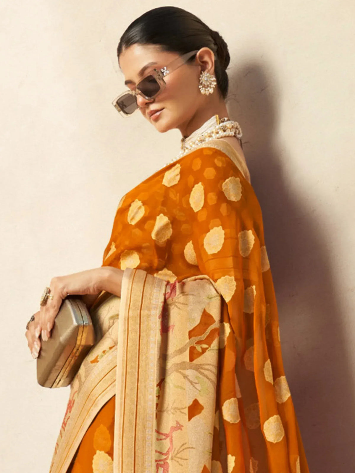 Woman in orange floral saree with pearl jewelry and sunglasses, elegant ethnic wear