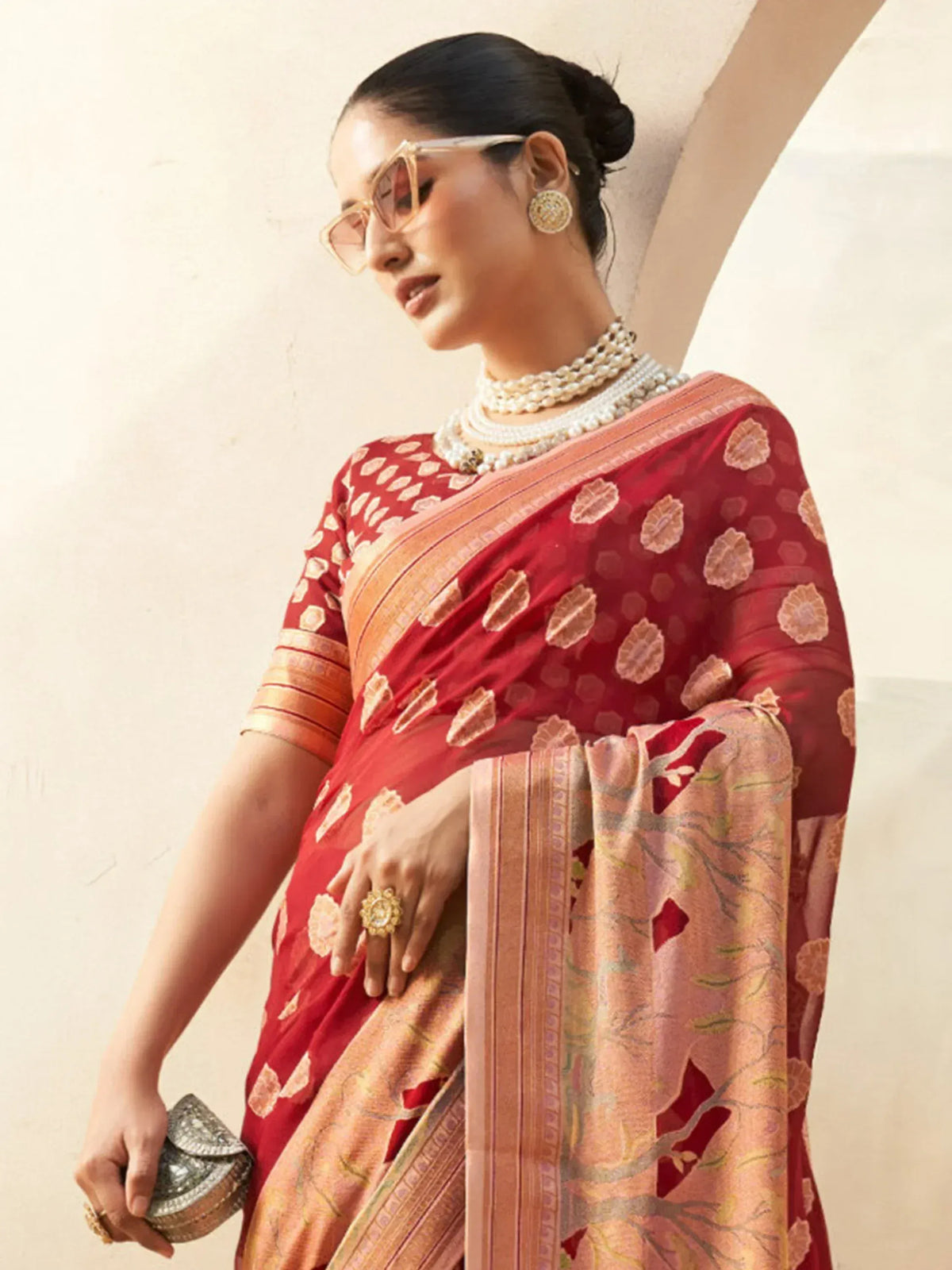 Red and peach designer saree with floral motifs, paired with pearl jewelry and statement sunglasses