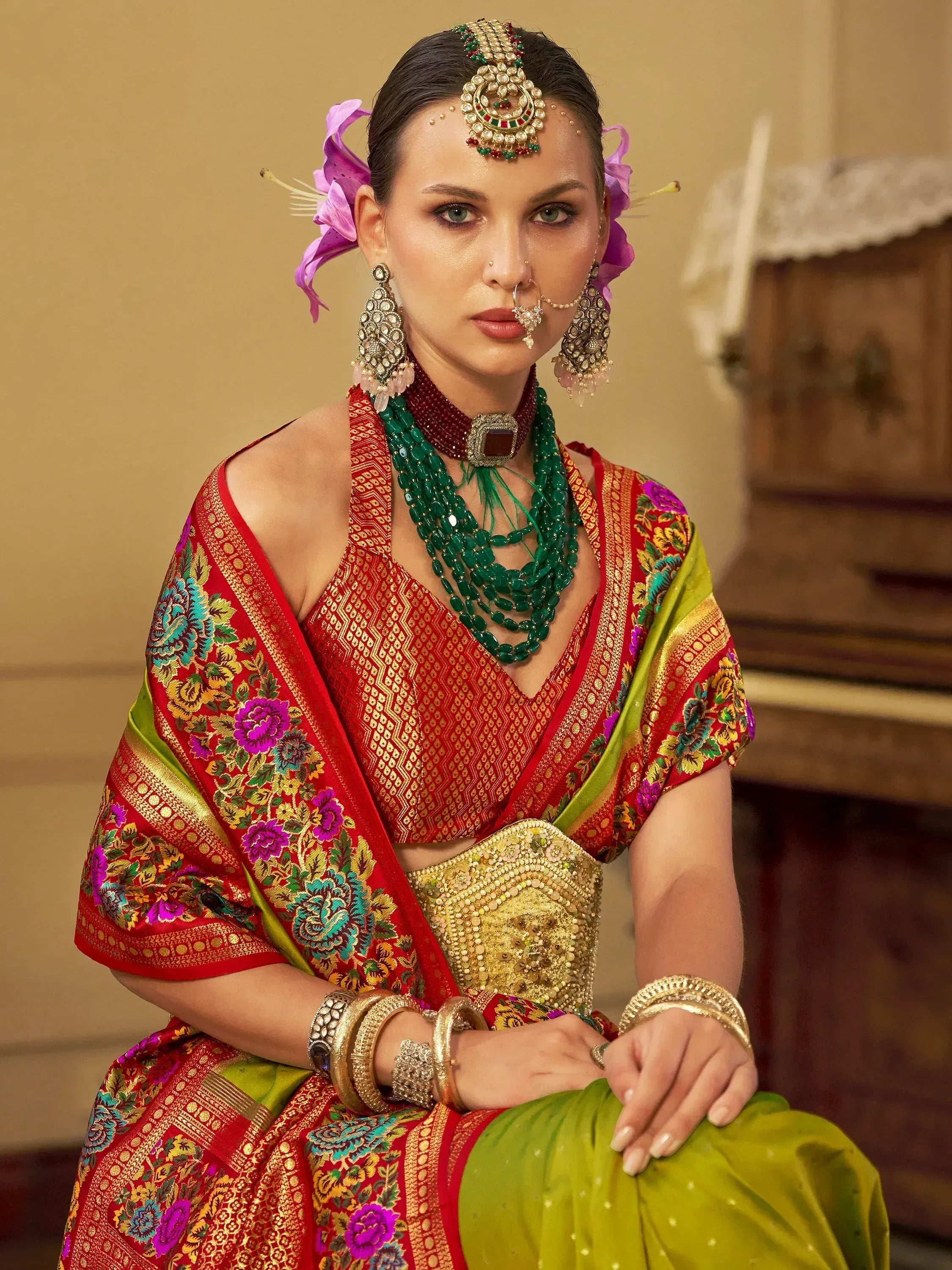 Woman in vibrant red and green Indian ethnic lehenga choli with floral embroidery, traditional jewelry, and floral hair accessories.