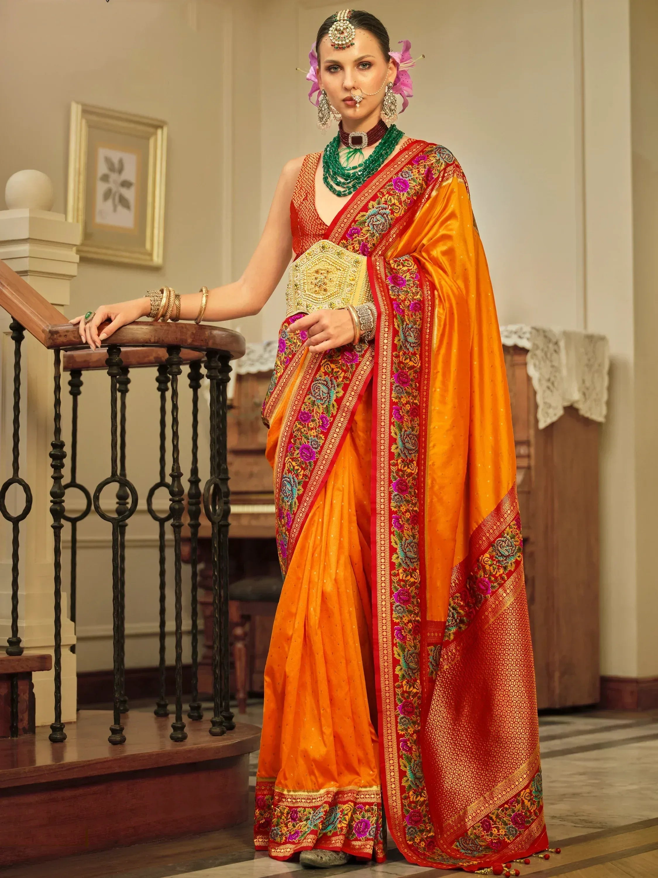 Vibrant orange and red embroidered saree with floral border, paired with traditional Indian jewelry and floral hair accessories.