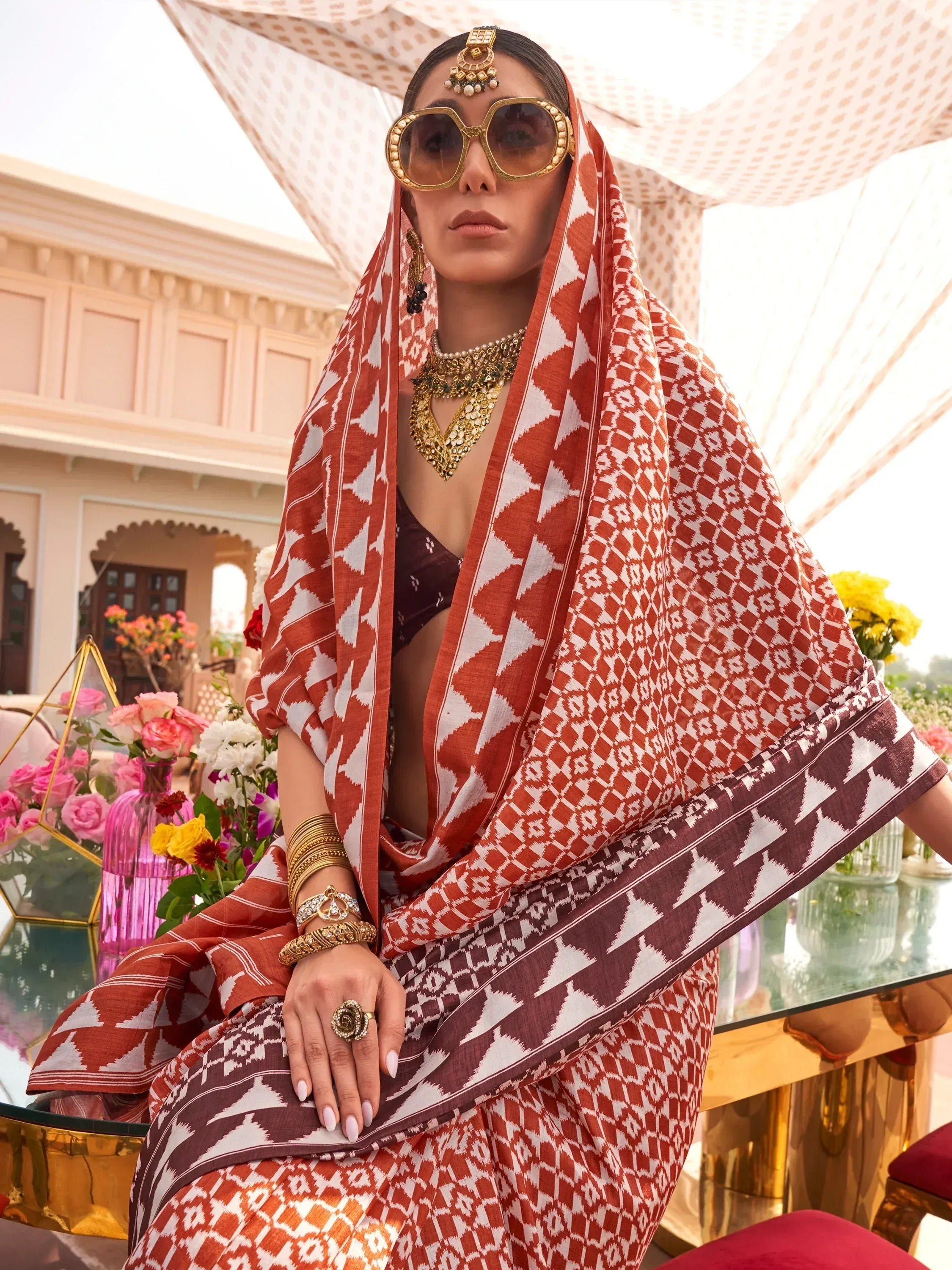 Woman in ethnic Indian saree with geometric print, gold jewelry, and statement sunglasses