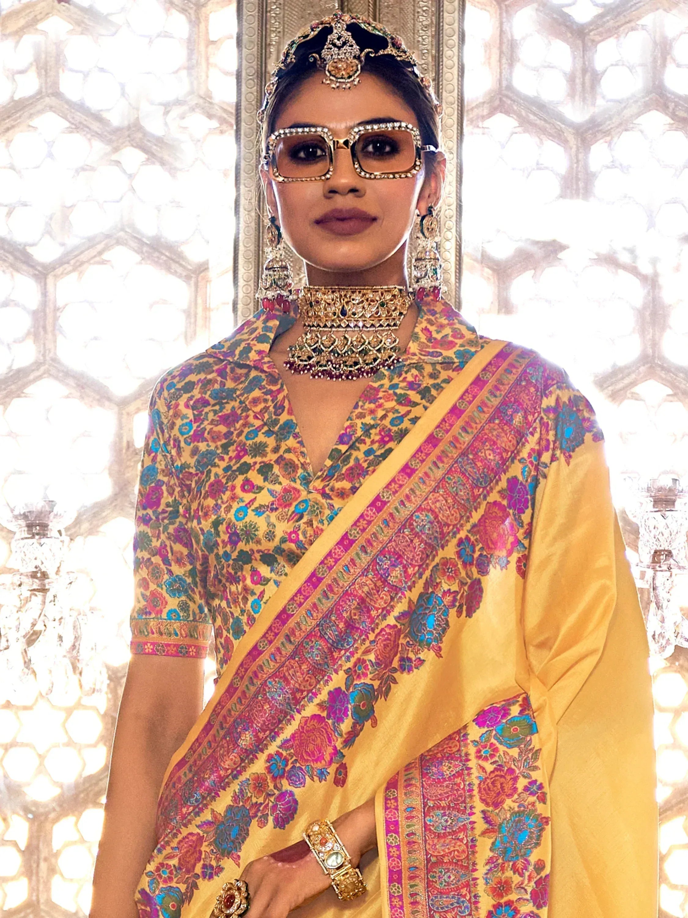 Woman in vibrant yellow floral saree with heavy ethnic jewelry and statement sunglasses, traditional Indian attire