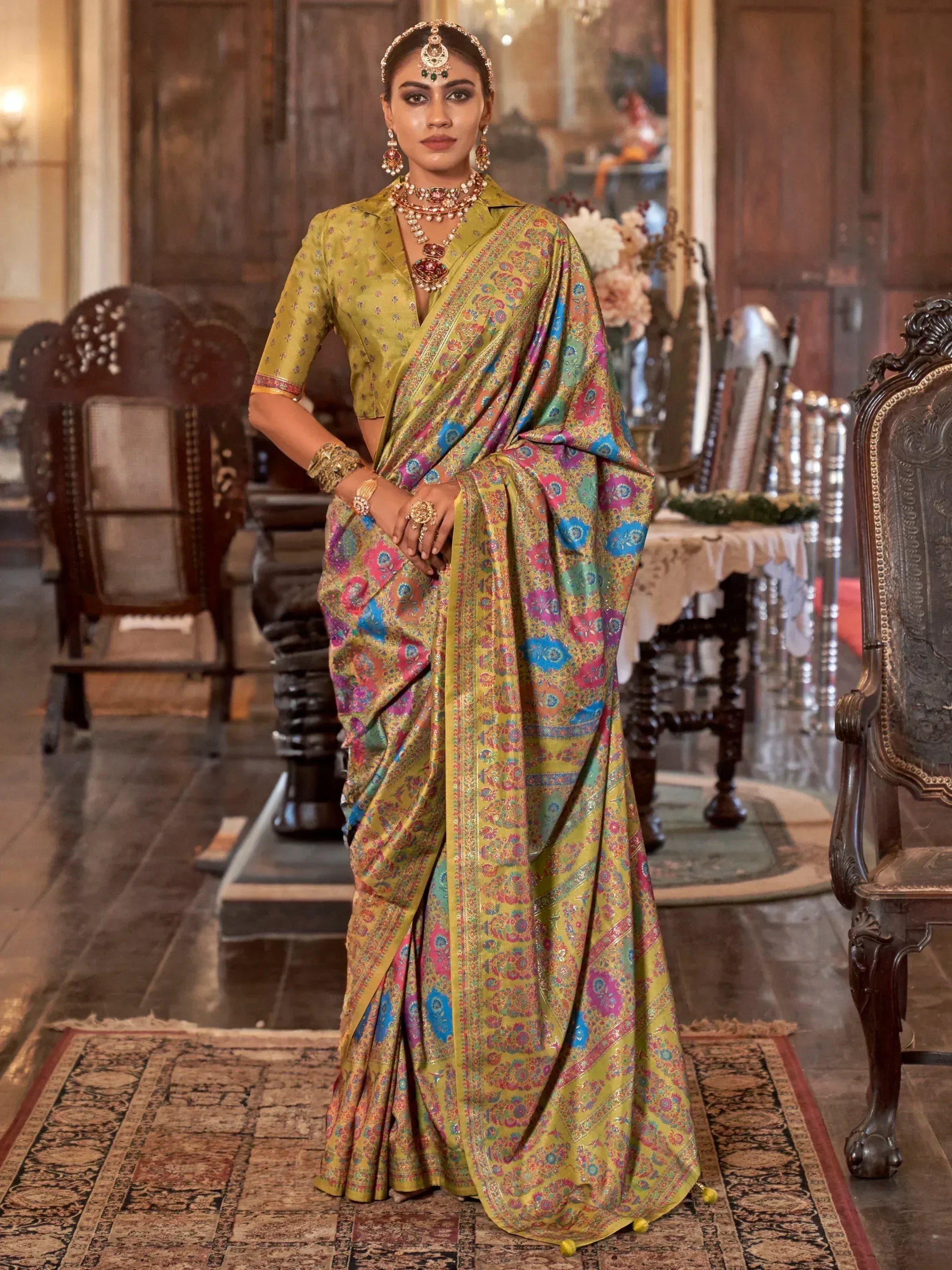 Woman in vibrant floral saree with gold blouse, traditional jewelry, standing in ornate room