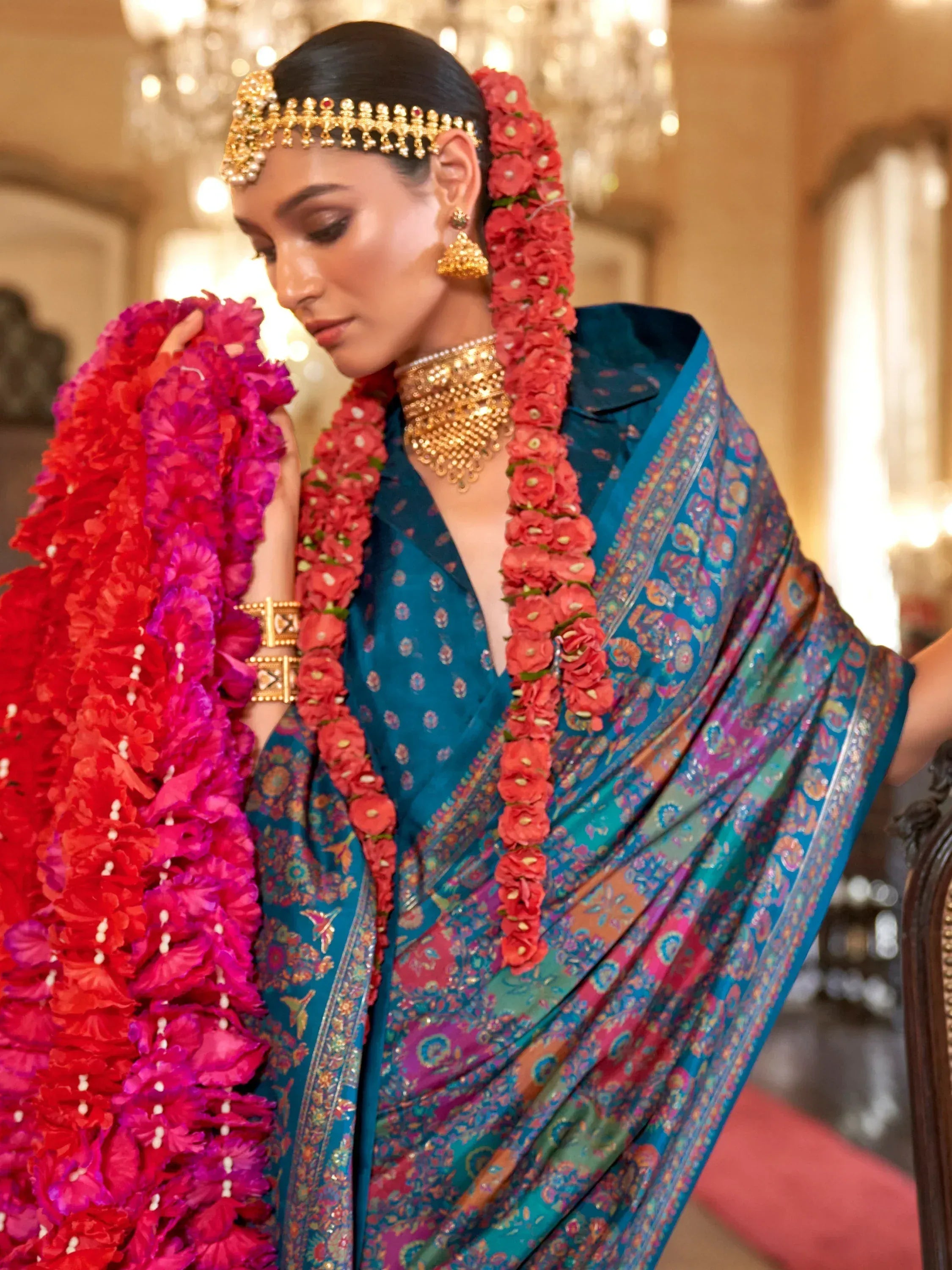 Elegant woman in blue floral saree with gold jewelry and vibrant flower garlands