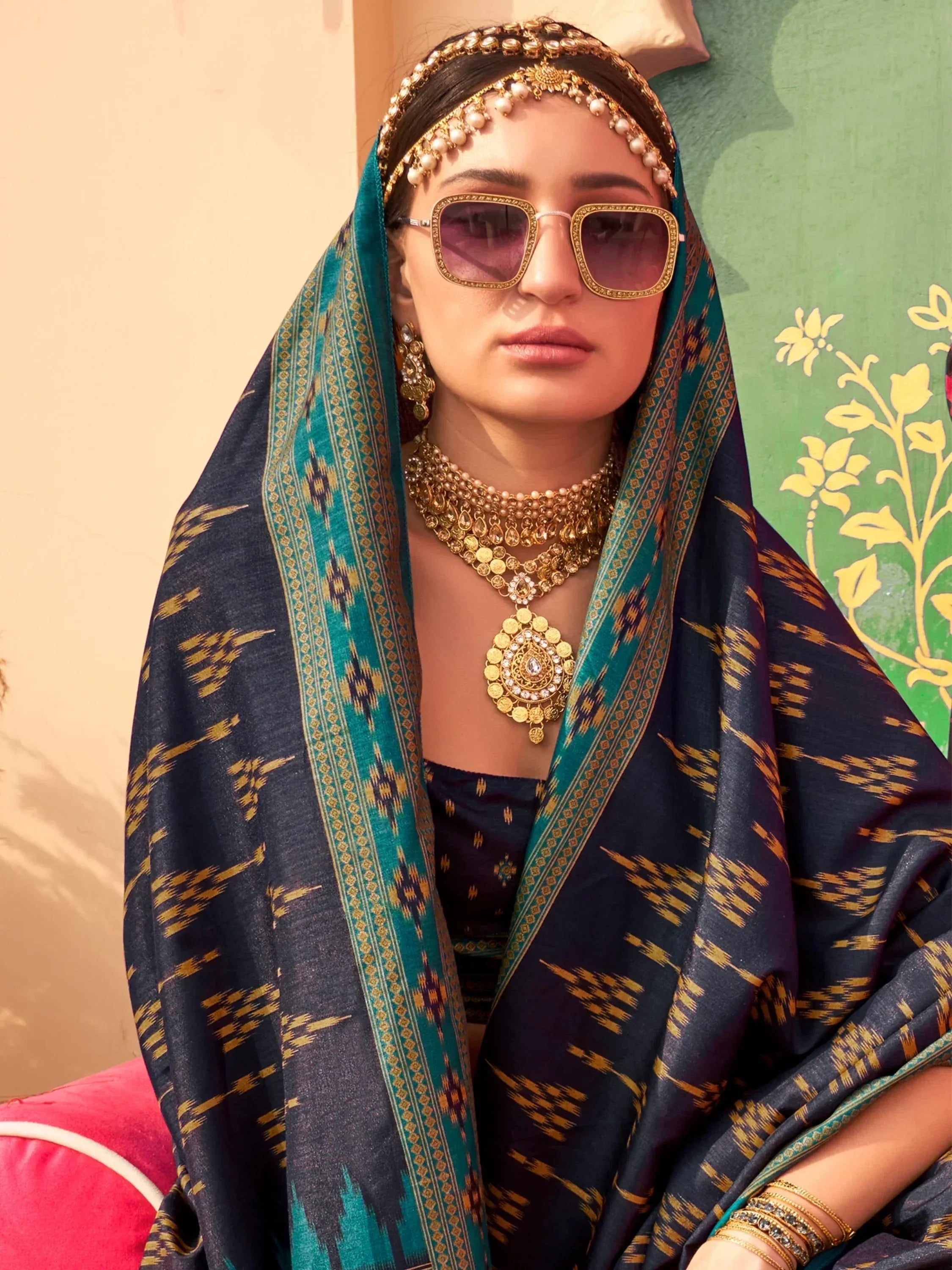 Woman in navy blue and teal ikat saree with gold jewelry and sunglasses, Indian ethnic wear