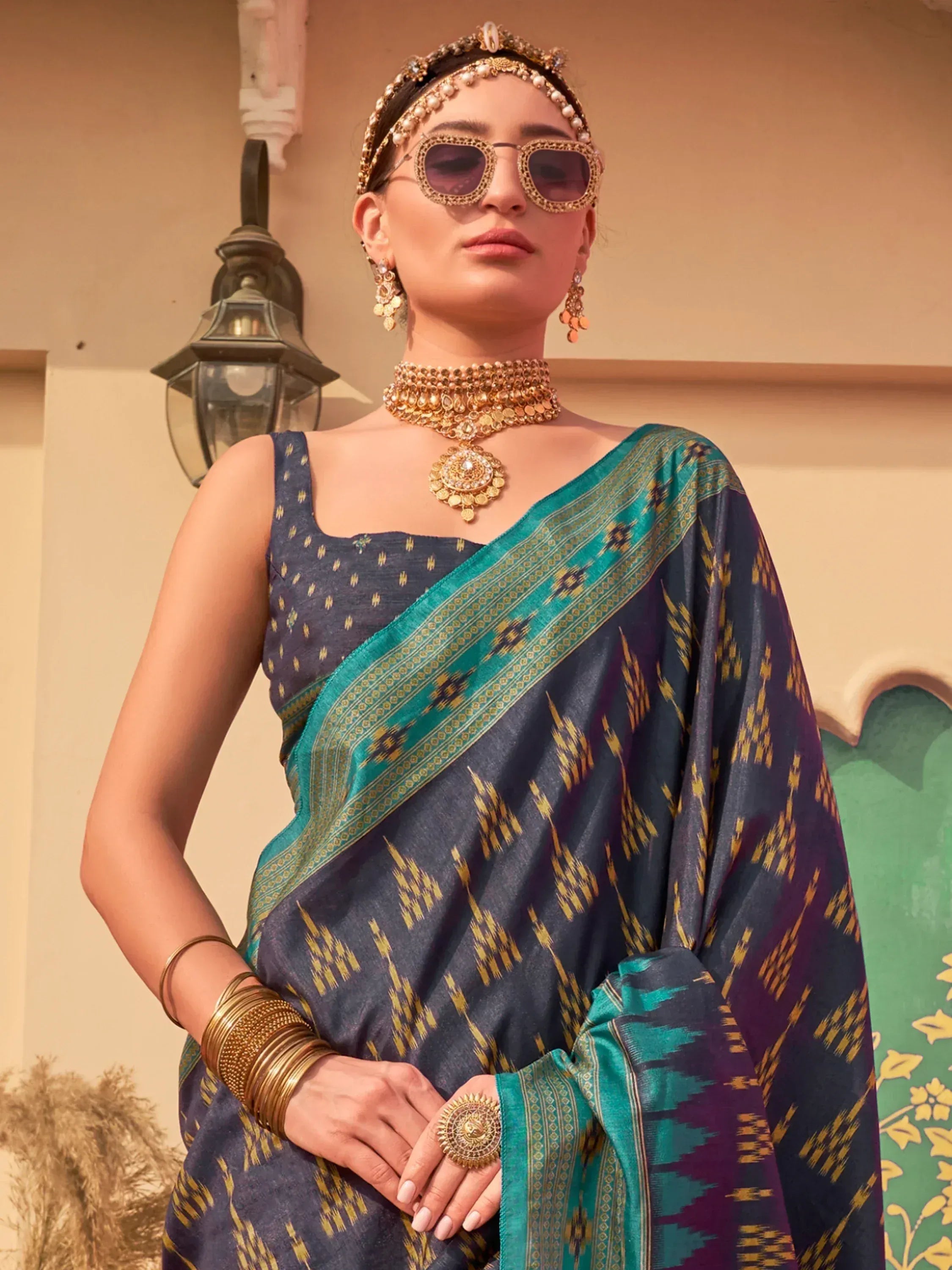 Woman in navy blue and teal ikat saree with gold jewelry and sunglasses, ethnic Indian wear