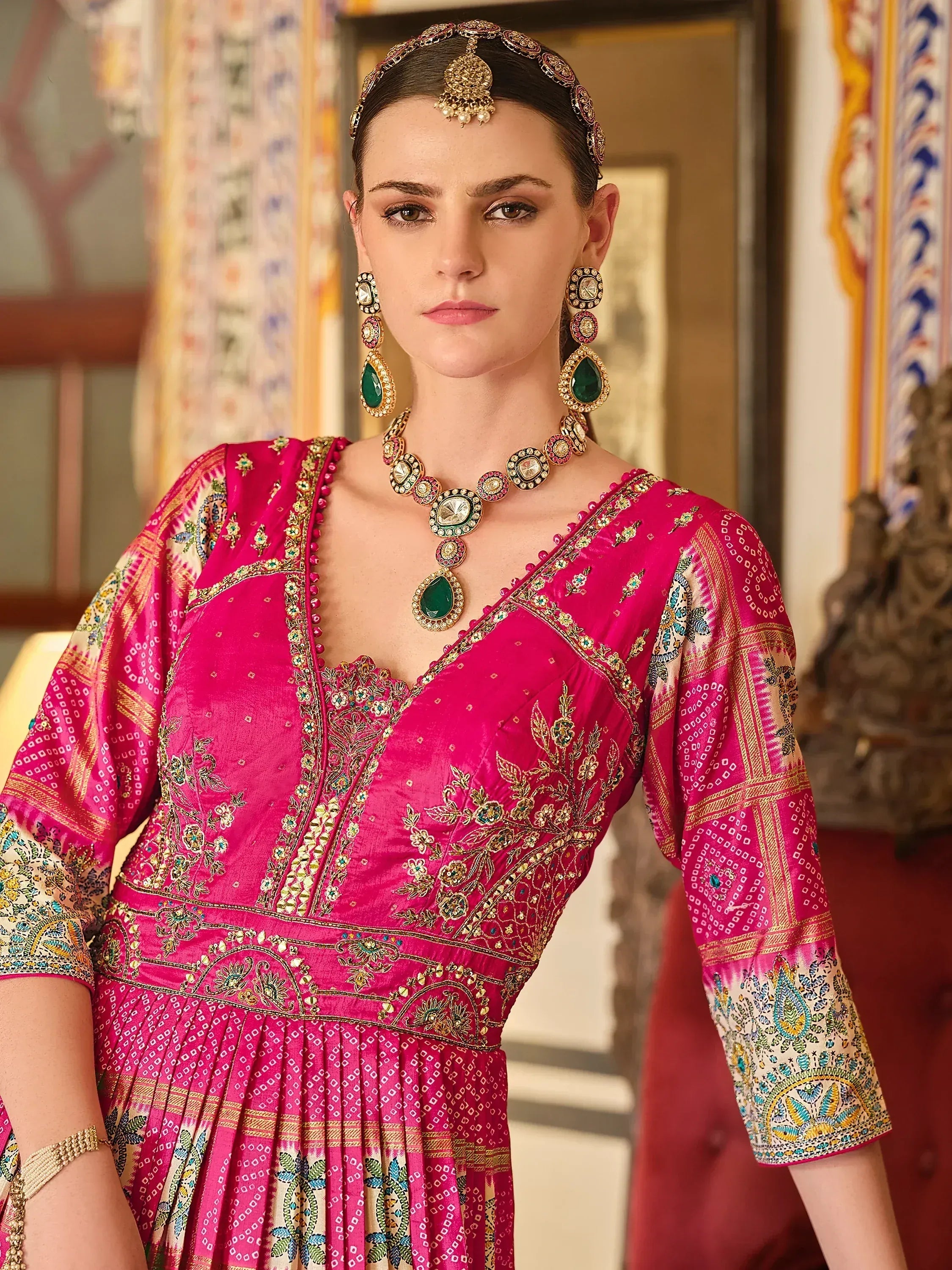 Pink embroidered ethnic gown with gold detailing, paired with traditional Indian jewelry for festive occasions.