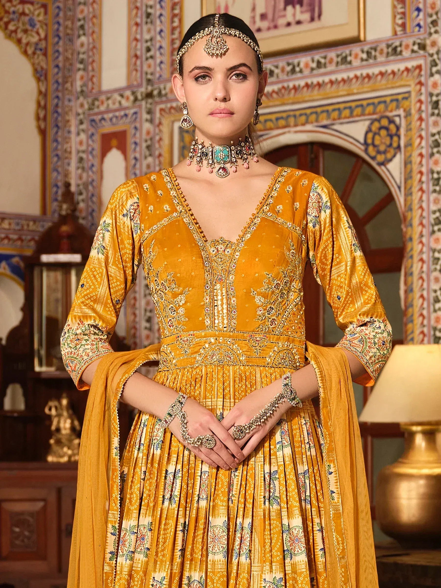 Yellow embroidered Indian anarkali suit with traditional jewelry and ethnic backdrop