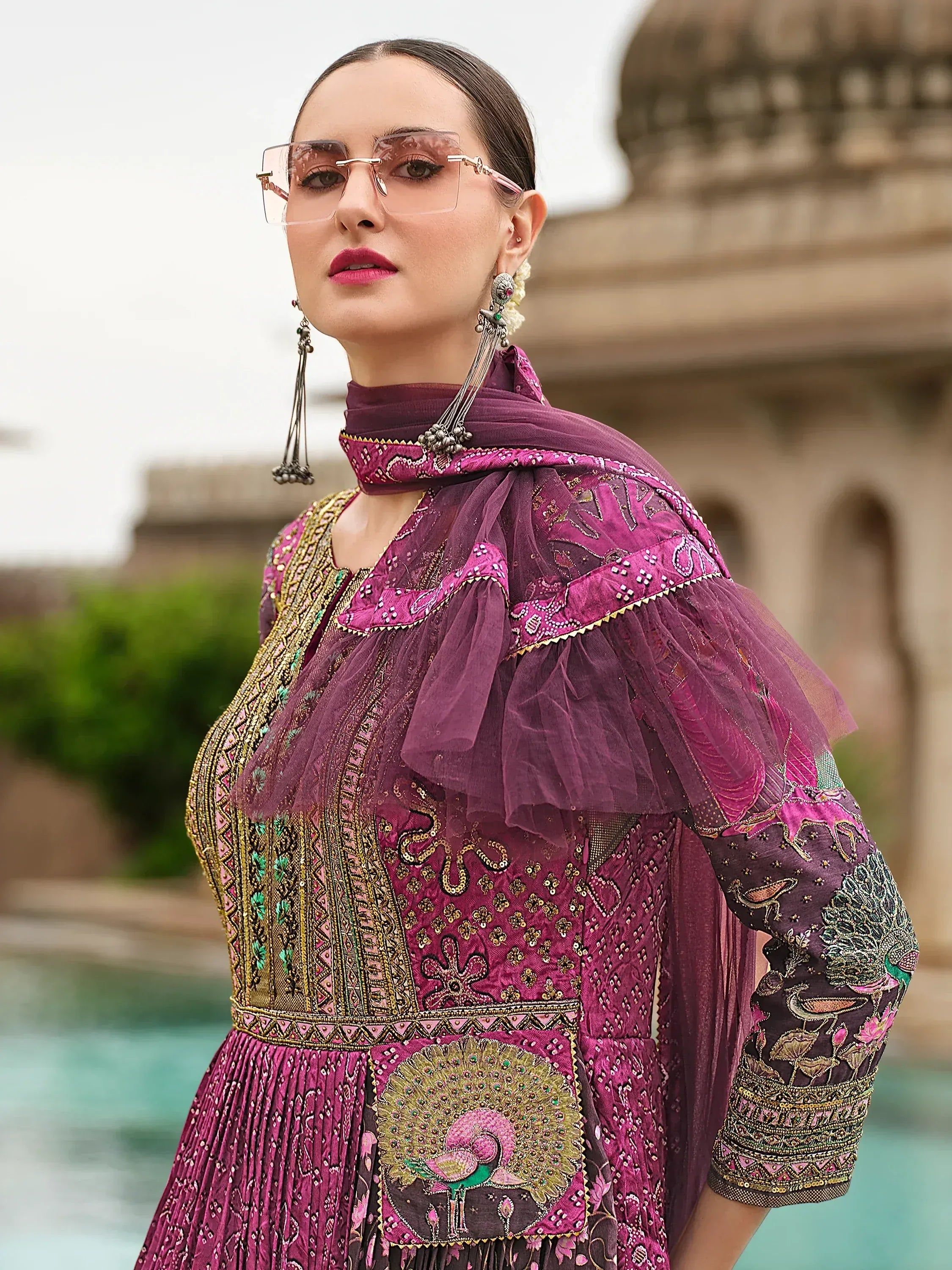 Elegant purple embroidered ethnic gown with peacock motif, tulle sleeves, and statement jewelry for festive occasions