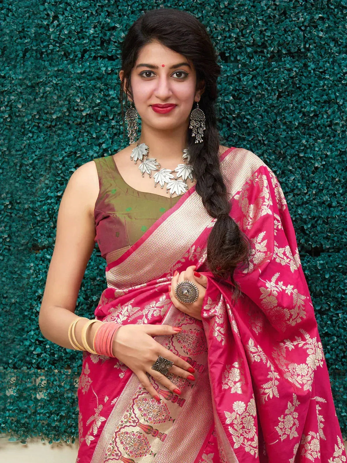 Woman in vibrant pink floral saree with gold border, olive green blouse, and traditional jewelry
