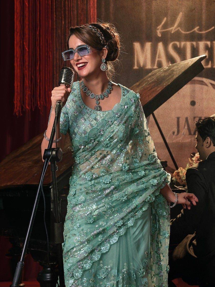 Woman in mint green designer saree with floral embroidery singing into vintage mic at jazz event