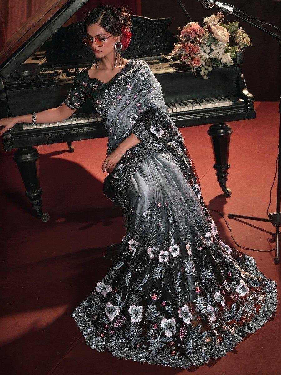 Elegant black floral embroidered saree with sheer overlay, styled with sunglasses and red hair accessory near grand piano