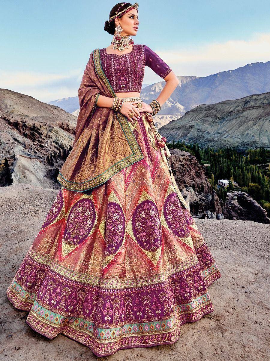 Woman in designer lehenga choli with intricate embroidery, standing against mountain backdrop