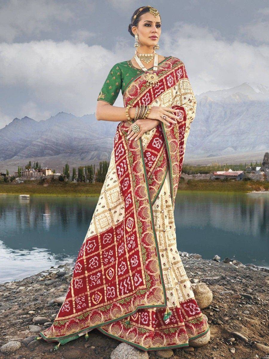Woman in designer ethnic saree with red and green embroidery, standing by lake with mountains