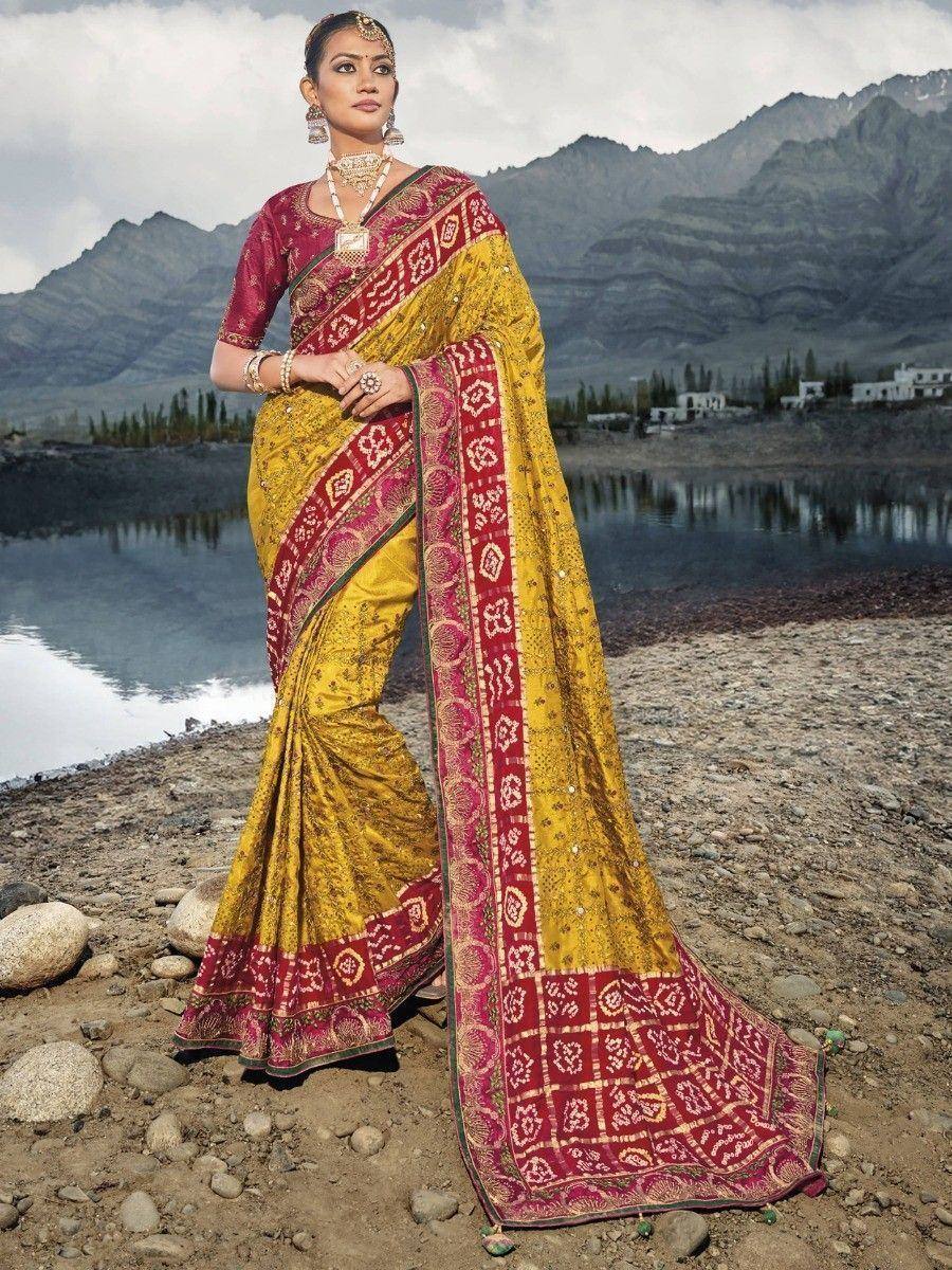 Yellow and red designer saree with intricate embroidery, worn by woman near mountain lake