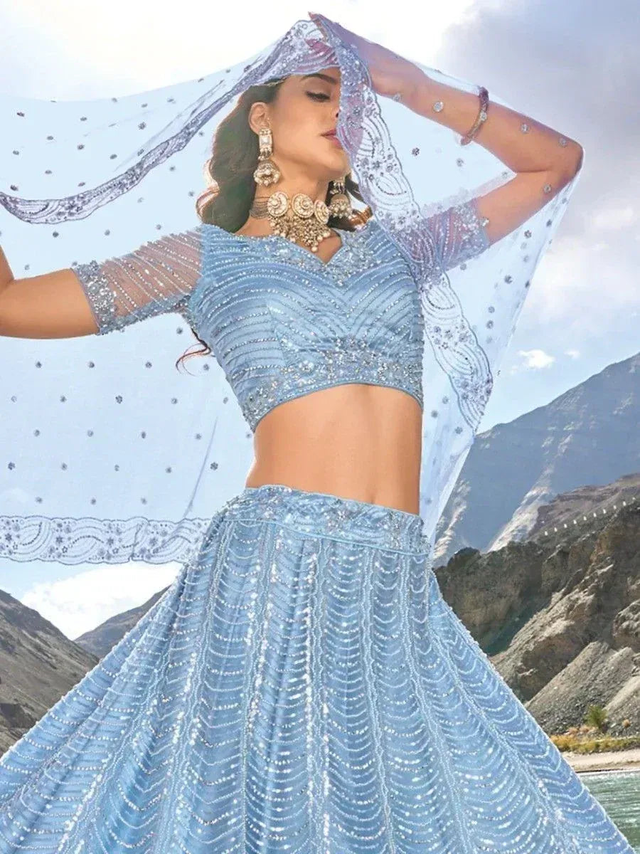 Light blue designer lehenga choli with intricate beadwork, sheer dupatta, and mountain backdrop