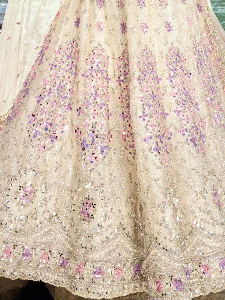 Cream lehenga with pink and purple floral mirror work, perfect for Indian weddings and festive occasions.