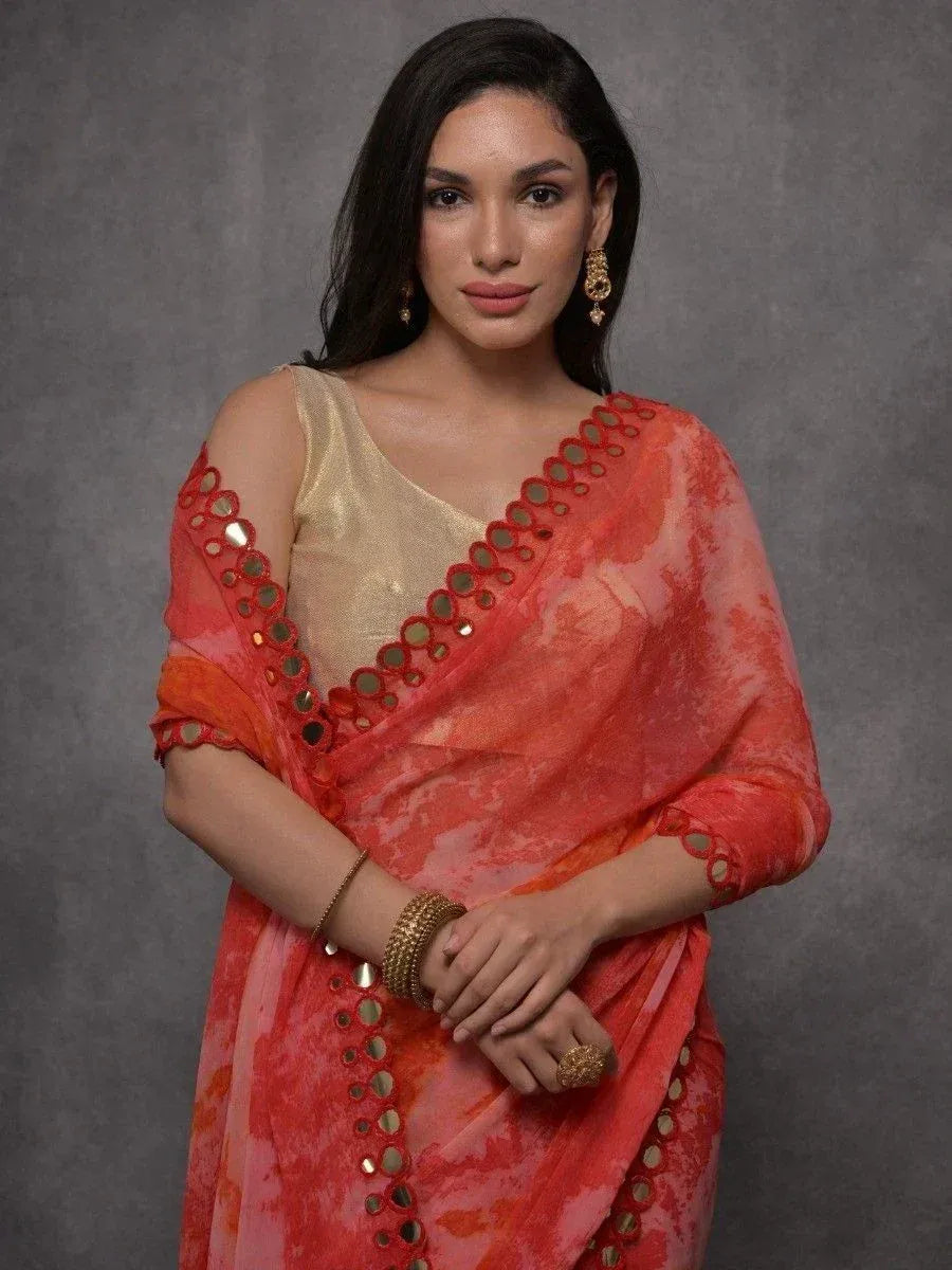 Woman in vibrant orange saree with mirror work and gold blouse, styled with ethnic jewelry for festive occasions