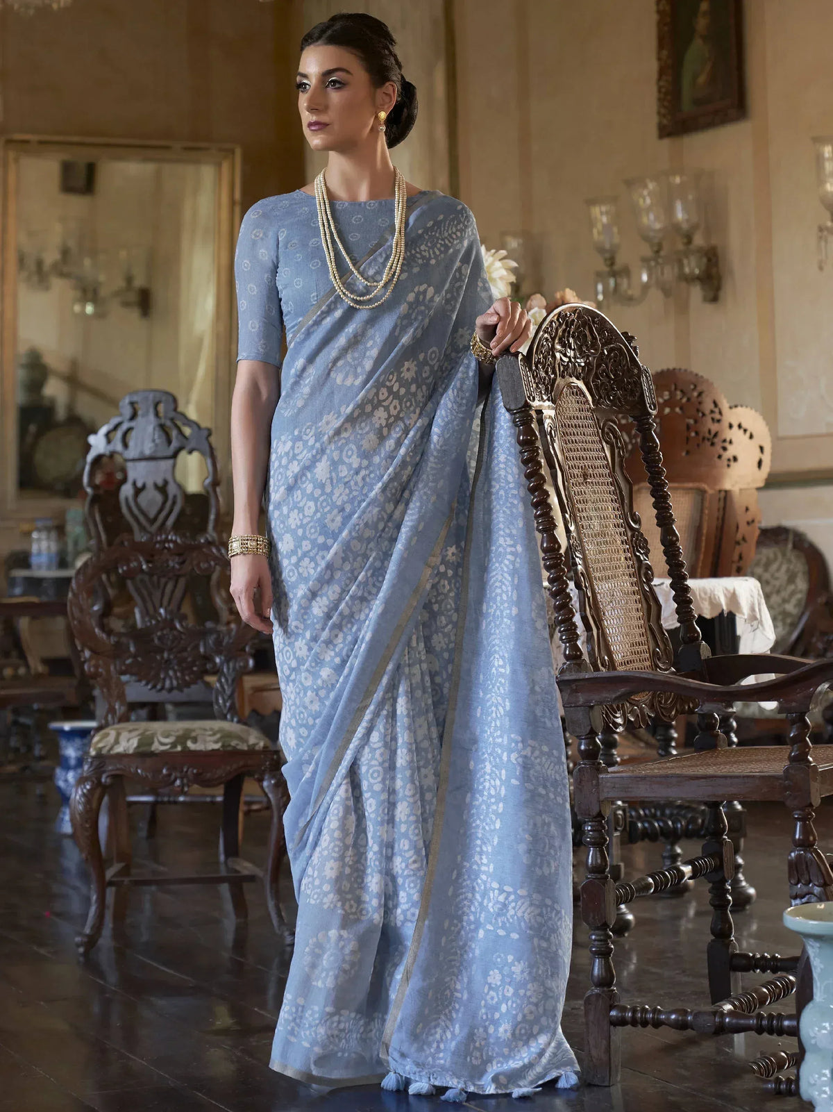Elegant light blue floral saree with gold border, styled with pearl necklace and traditional jewelry for ethnic occasions.