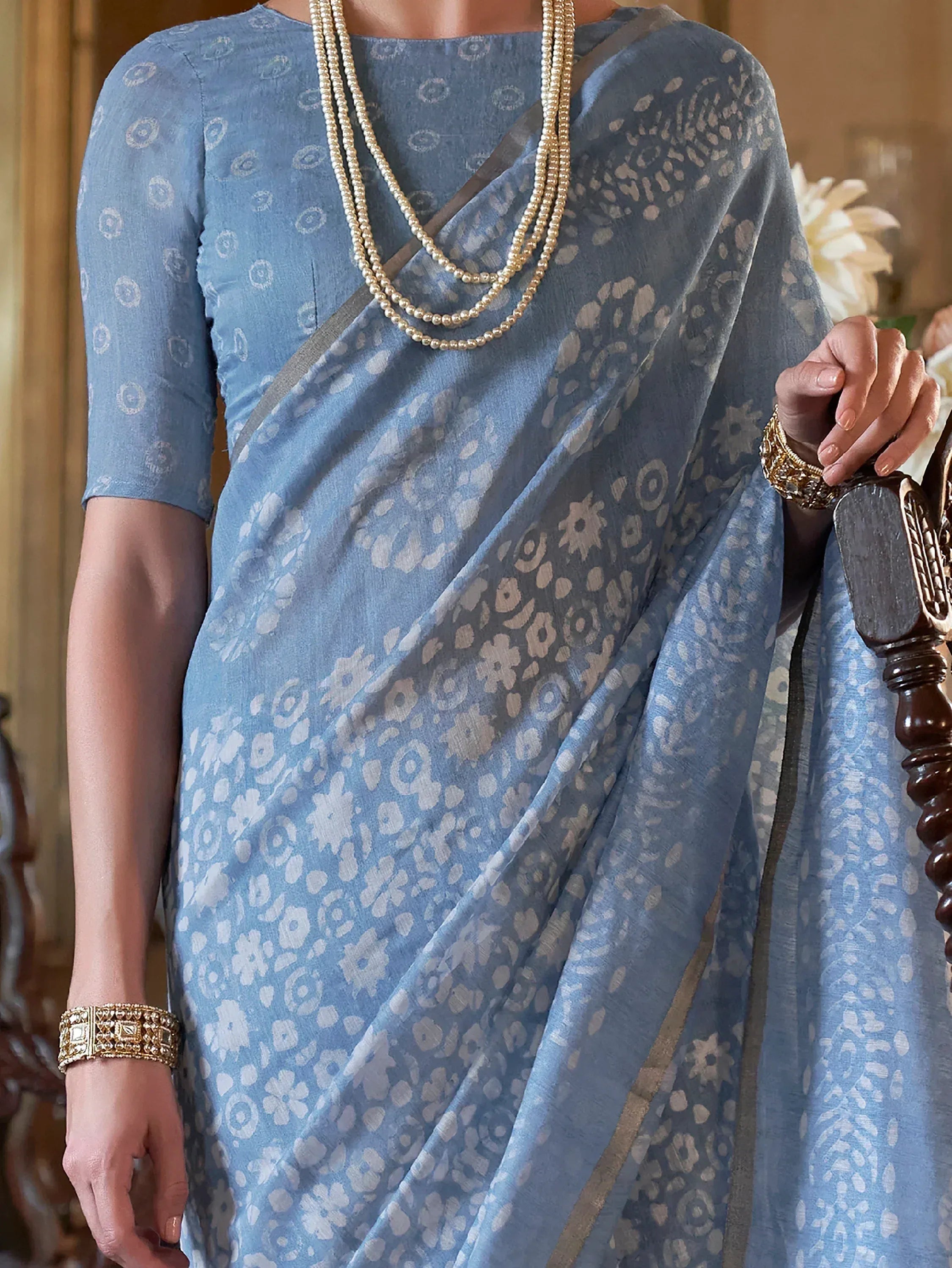 Blue floral printed saree with gold border, paired with pearl necklace and ethnic jewelry for traditional Indian wear