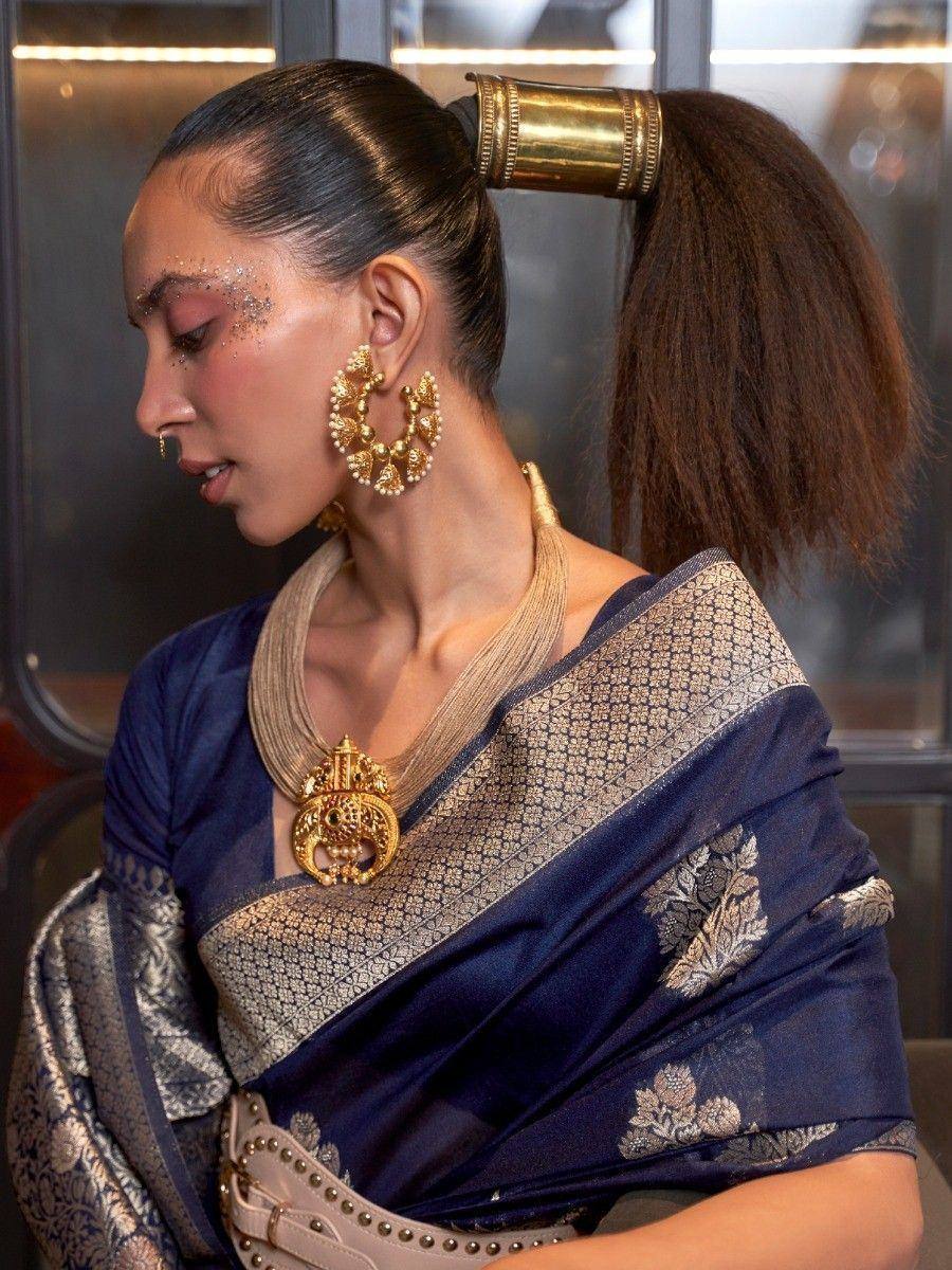 Woman in navy blue designer saree with gold embroidery, statement gold jewelry, and traditional hair accessory