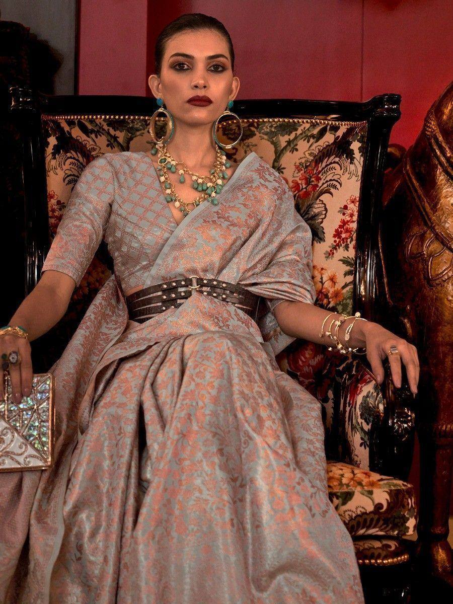 Elegant woman in designer ethnic gown with floral print, statement jewelry, and embellished clutch, seated on ornate chair