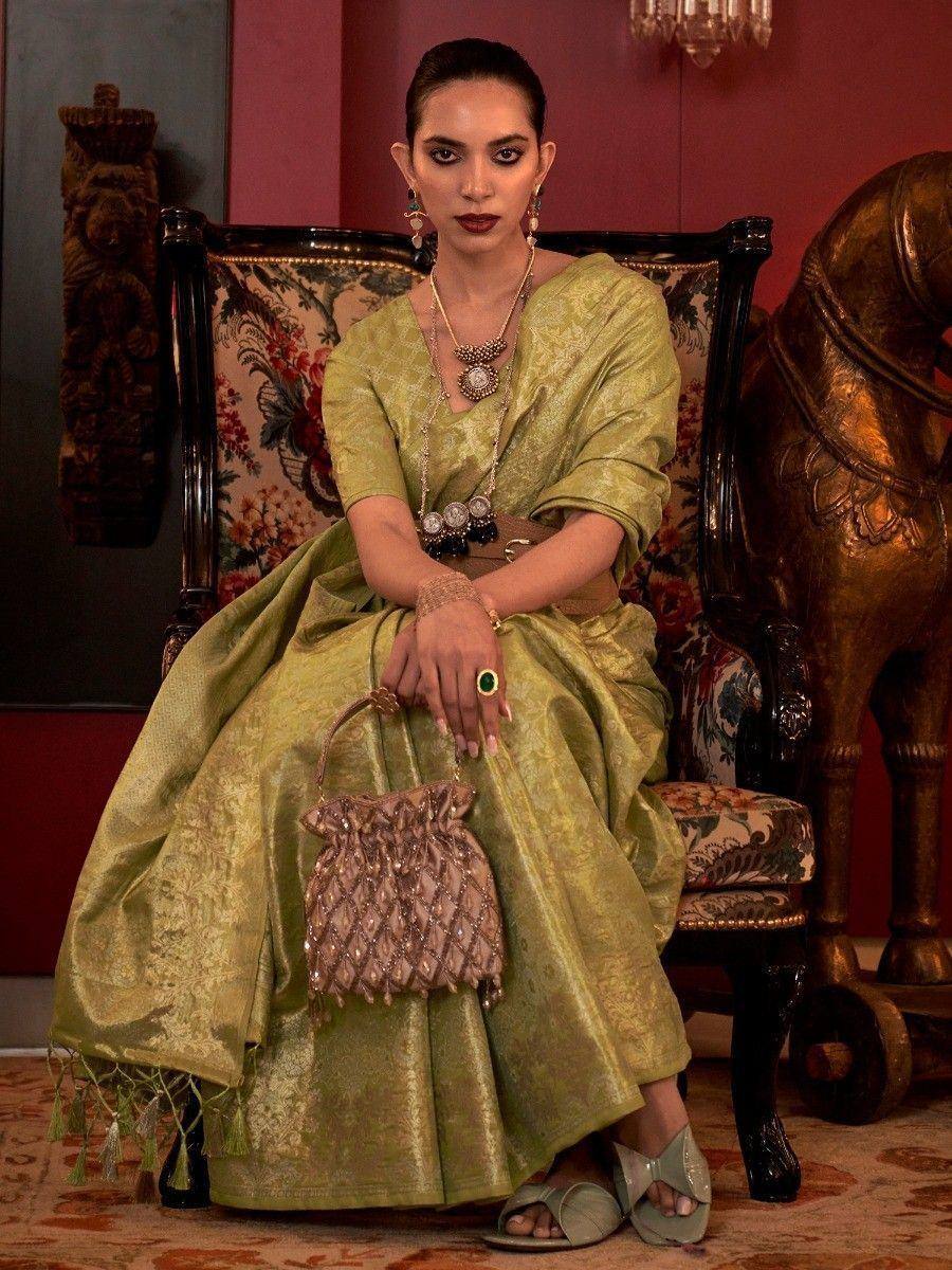 Elegant olive green ethnic gown with gold embroidery, paired with statement jewelry and a beaded handbag.