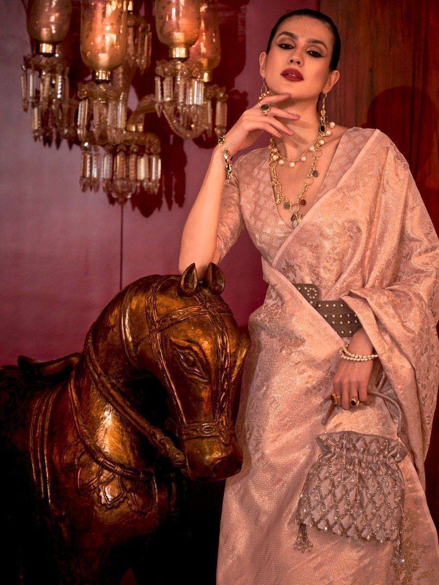 Elegant woman in designer ethnic gown with intricate embroidery, posing beside golden horse statue under chandelier