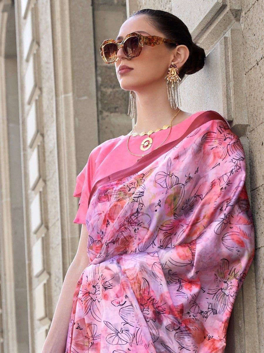 Woman in pink floral saree with gold jewelry and sunglasses, leaning against stone wall