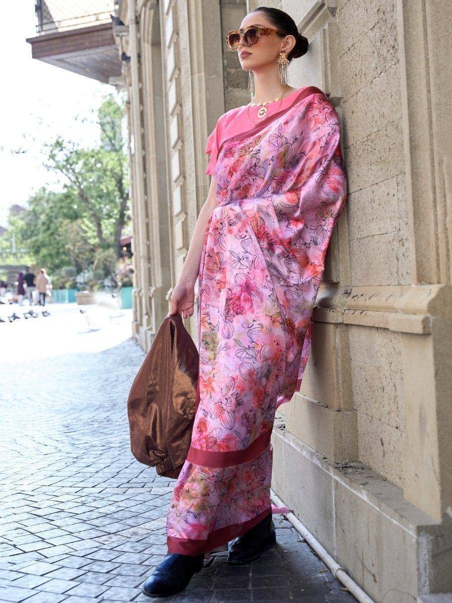 Woman in pink floral printed saree with modern blouse, stylish sunglasses, and gold jewelry, leaning against stone wall