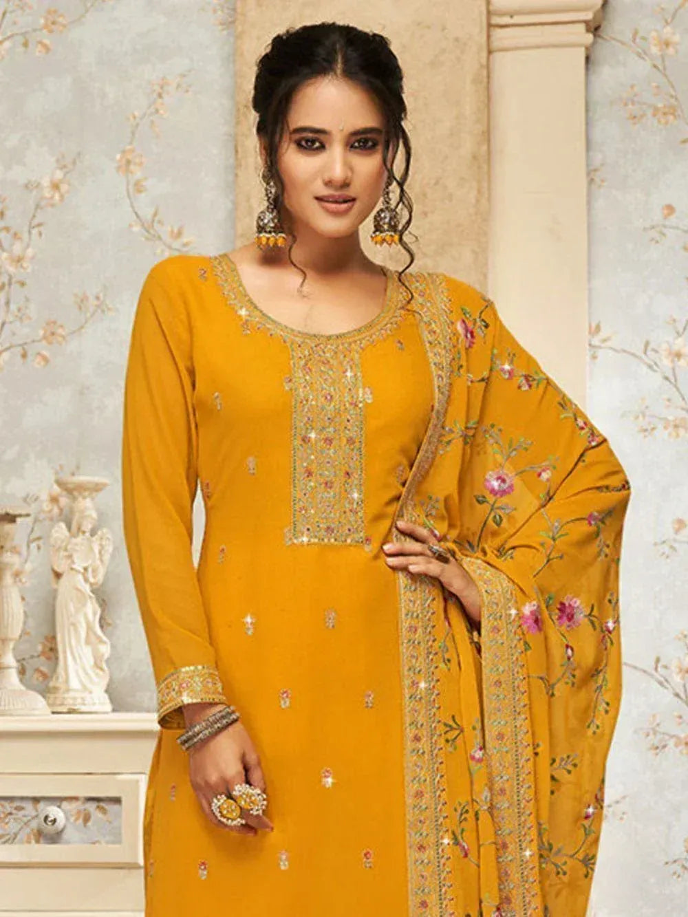 Woman in mustard yellow embroidered salwar kameez with floral dupatta and jewelry