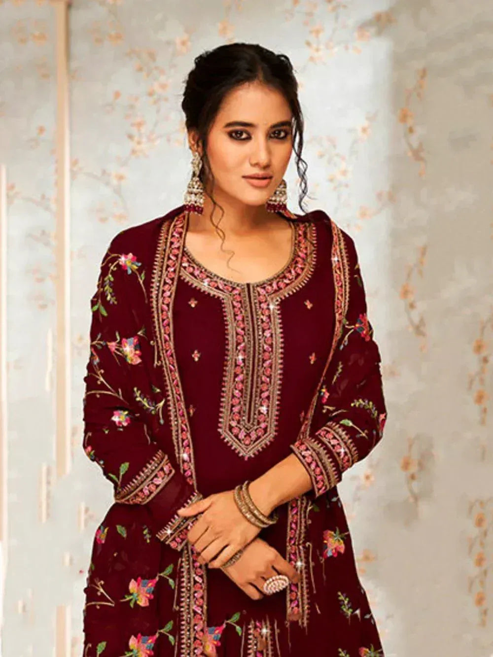 Woman wearing maroon embroidered salwar kameez with floral patterns and ethnic jewelry