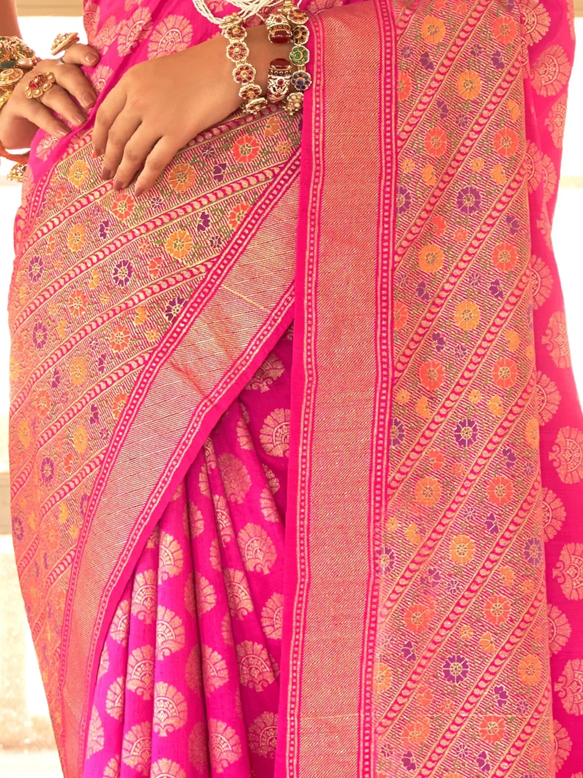 Vibrant pink Indian saree with intricate floral and geometric woven patterns, paired with traditional jewelry.